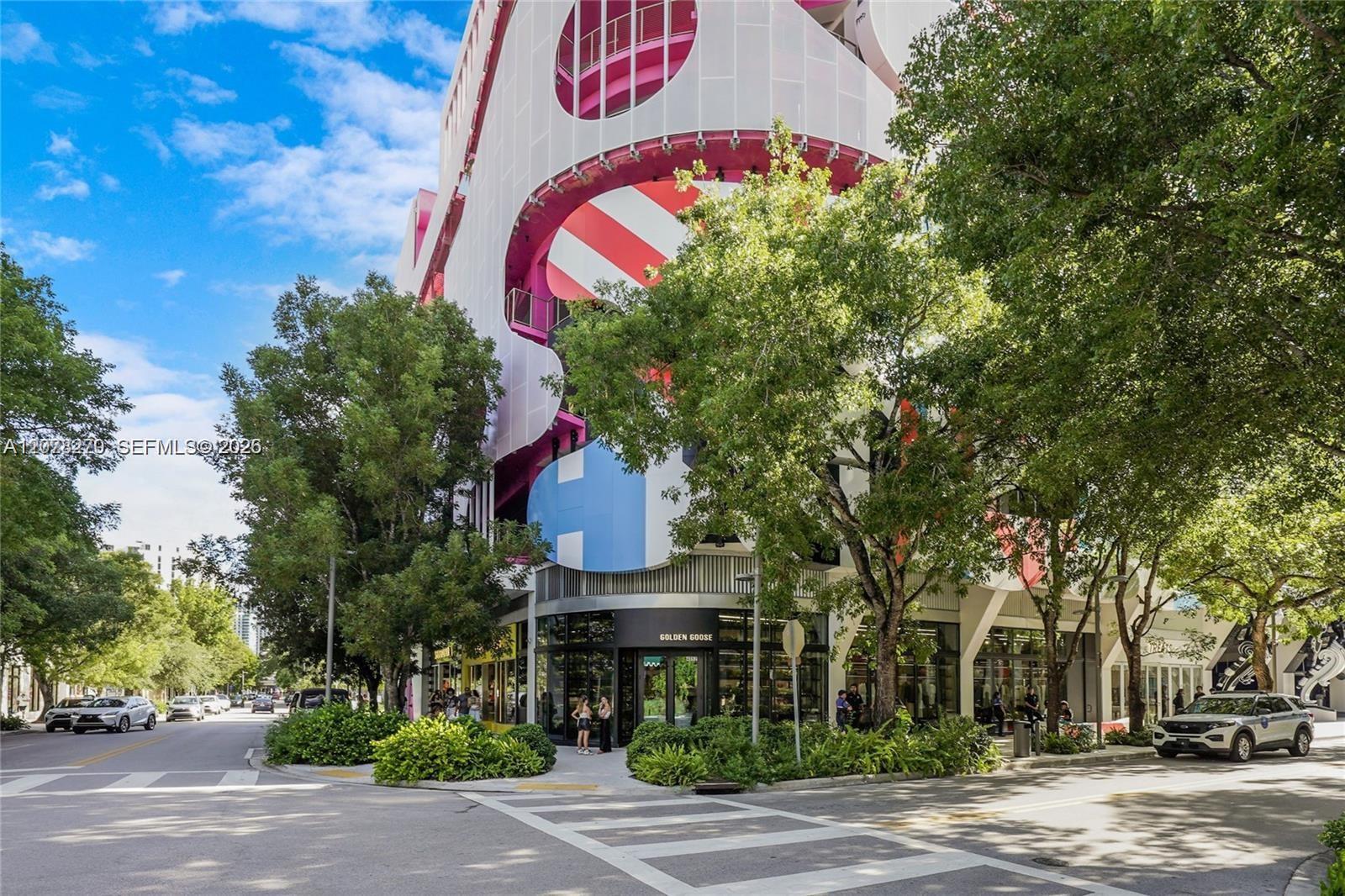Colorful sculptural building with pink and blue facade above a Golden Goose storefront on a tree-lined corner.