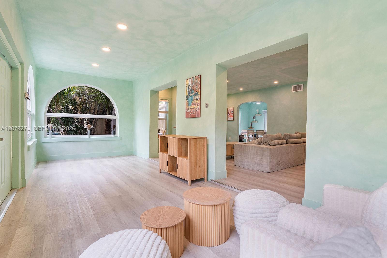 Mint-green living room with an arched window, pale wood floors, and rounded white chairs.