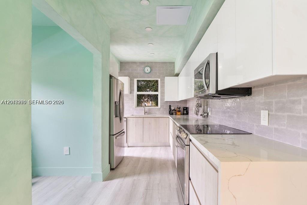 Renovated galley kitchen with white cabinets, stainless appliances, gray tile backsplash, and mint-green wall.