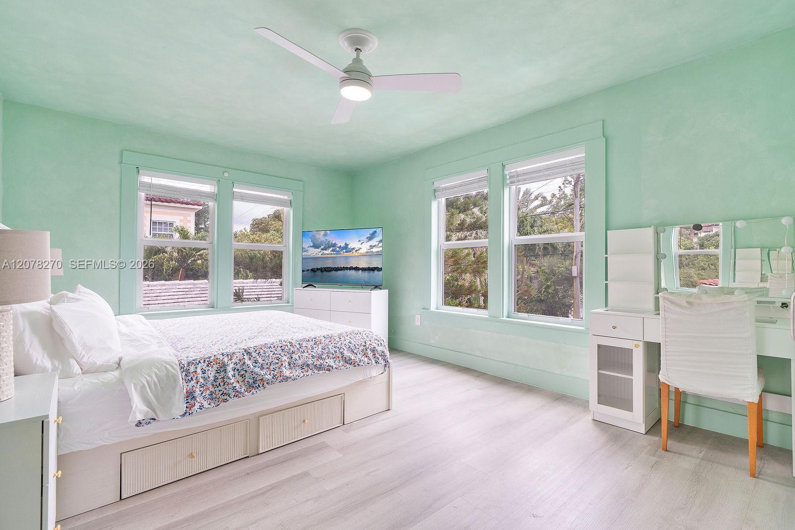 Mint-green bedroom with a white storage bed, floral bedding, four windows, and a mirrored vanity.