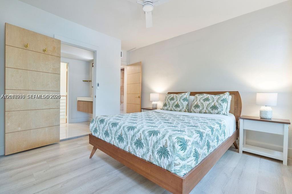 Bedroom with a wooden king bed, tropical palm-print bedding, and an adjoining bathroom doorway.
