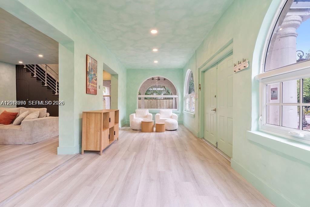 Mint-green entryway with arched windows, white chairs, pale wood floors, and a view into the living room.