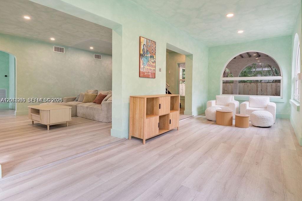 Mint-green living room with an arched window, pale wood floors, and two seating areas.