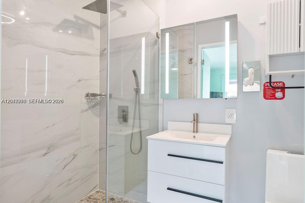 Modern bathroom with a glass shower, marble-look walls, and white floating vanity.