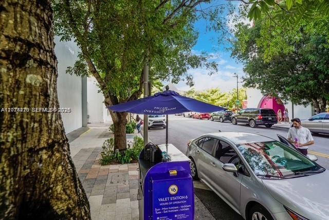 Street-side valet station beneath trees, beside a silver car and purple umbrella.