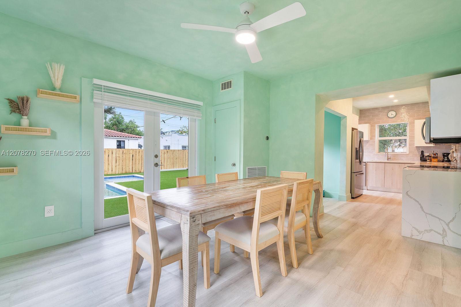 Dining area with mint-green walls and a wood table, opening to a backyard pool and modern kitchen.