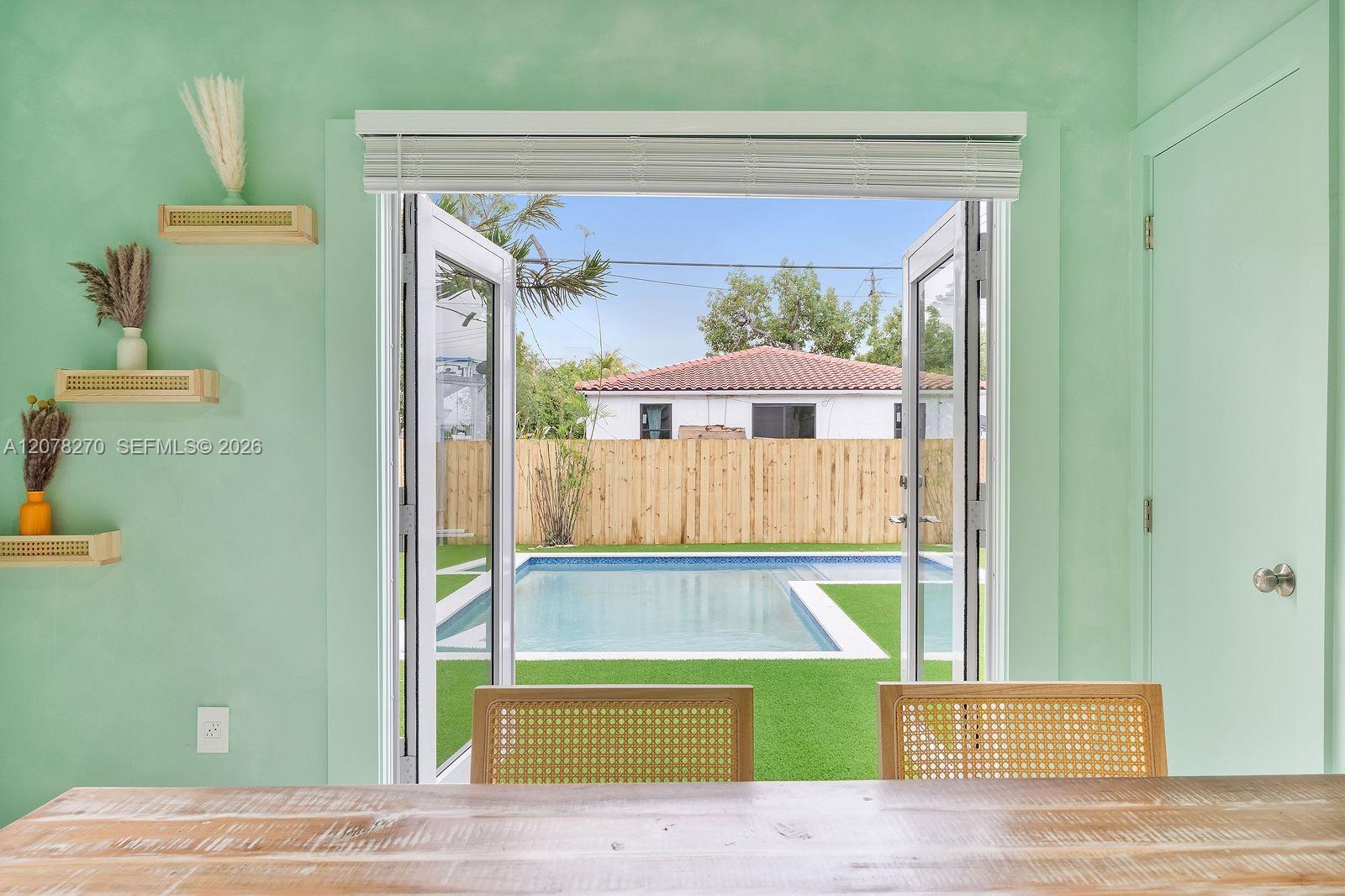 Dining area with mint-green walls and open doors overlooking a backyard pool.