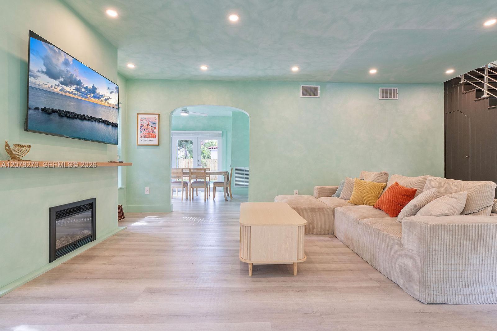 Mint-green living room with a cream sectional, fireplace, and arched opening to the dining area.