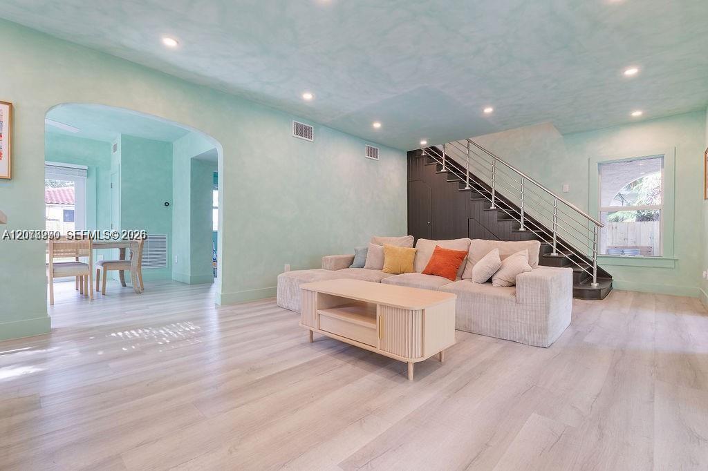 Furnished living room with a beige sofa, mint walls, and a metal-railed staircase.