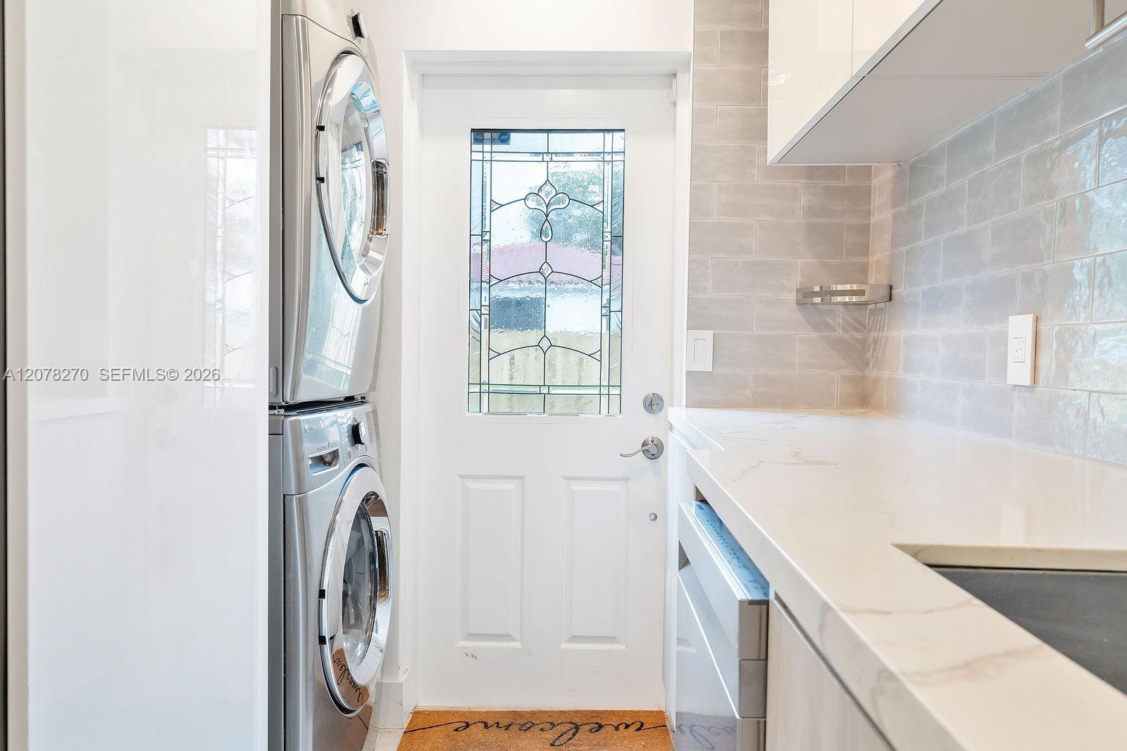 Laundry area with stacked washer and dryer beside a long white countertop and decorative glass door.