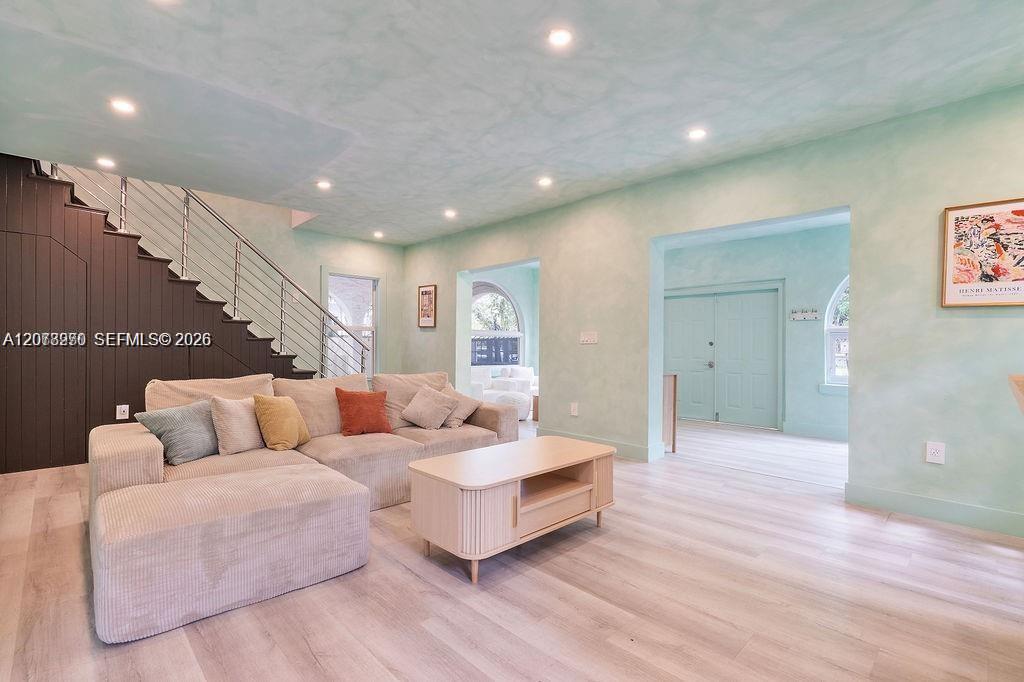 Living room with a beige sectional, pale wood coffee table, and dark staircase.