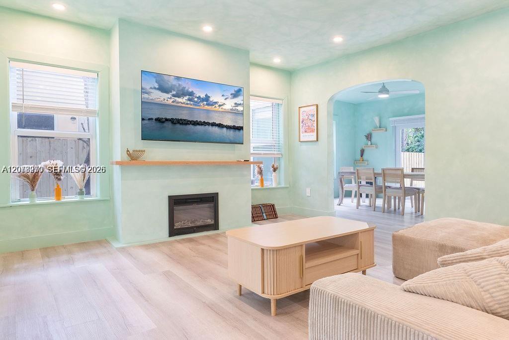 Living room with a fireplace, wall-mounted television, cream sofas, and an arched opening to the dining area.