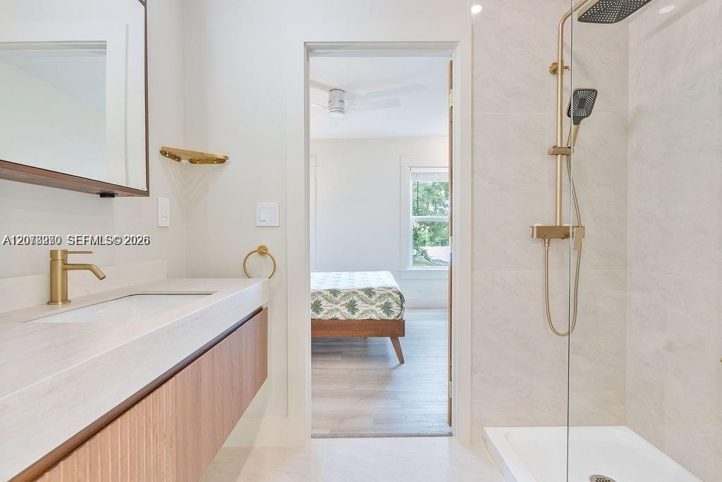 Bathroom with a wood-front vanity and gold fixtures beside a glass-enclosed shower.