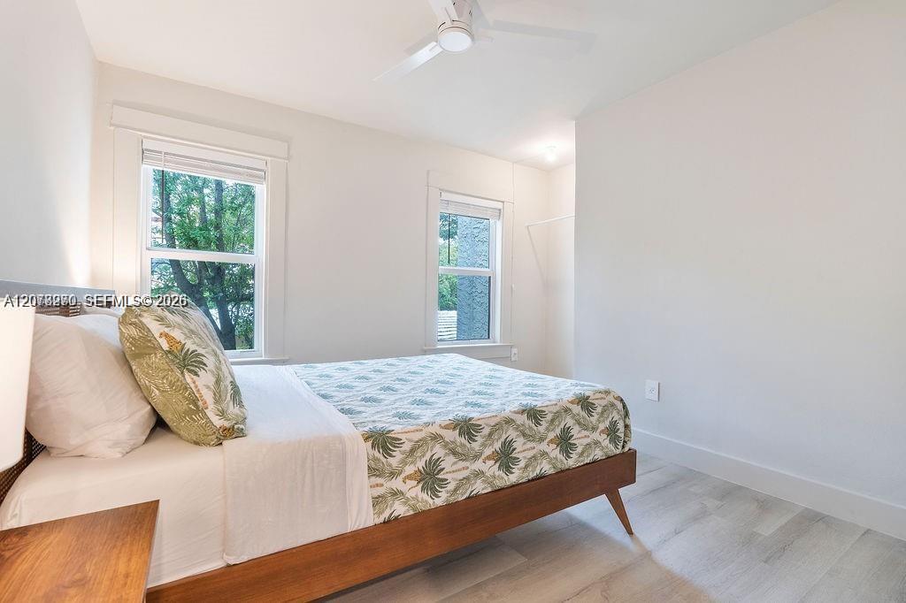 Bedroom with a low wooden bed, palm-print bedding, and two windows overlooking trees.