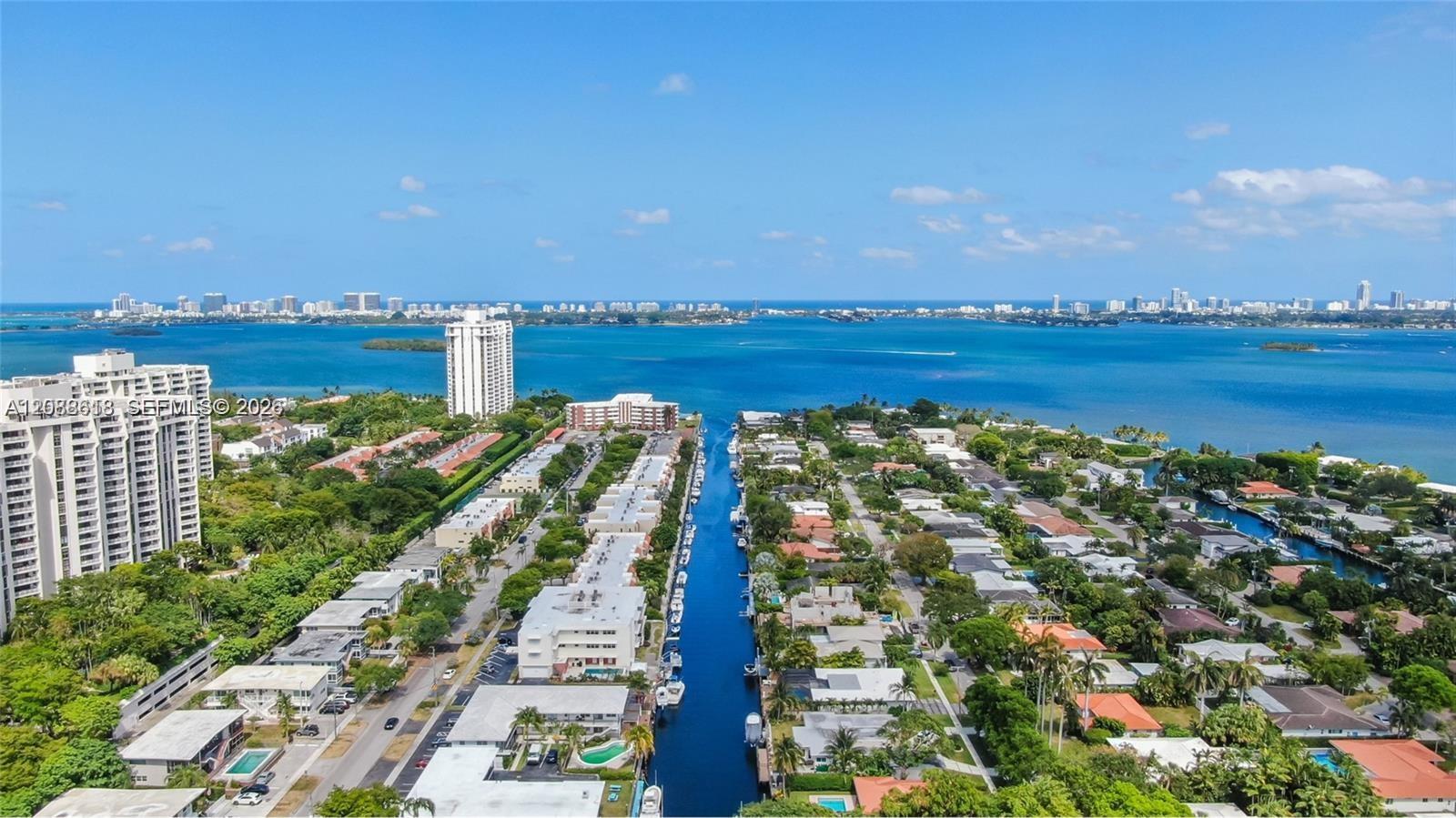 Aerial view of a waterfront neighborhood, with a canal leading toward the bay and distant skyline.