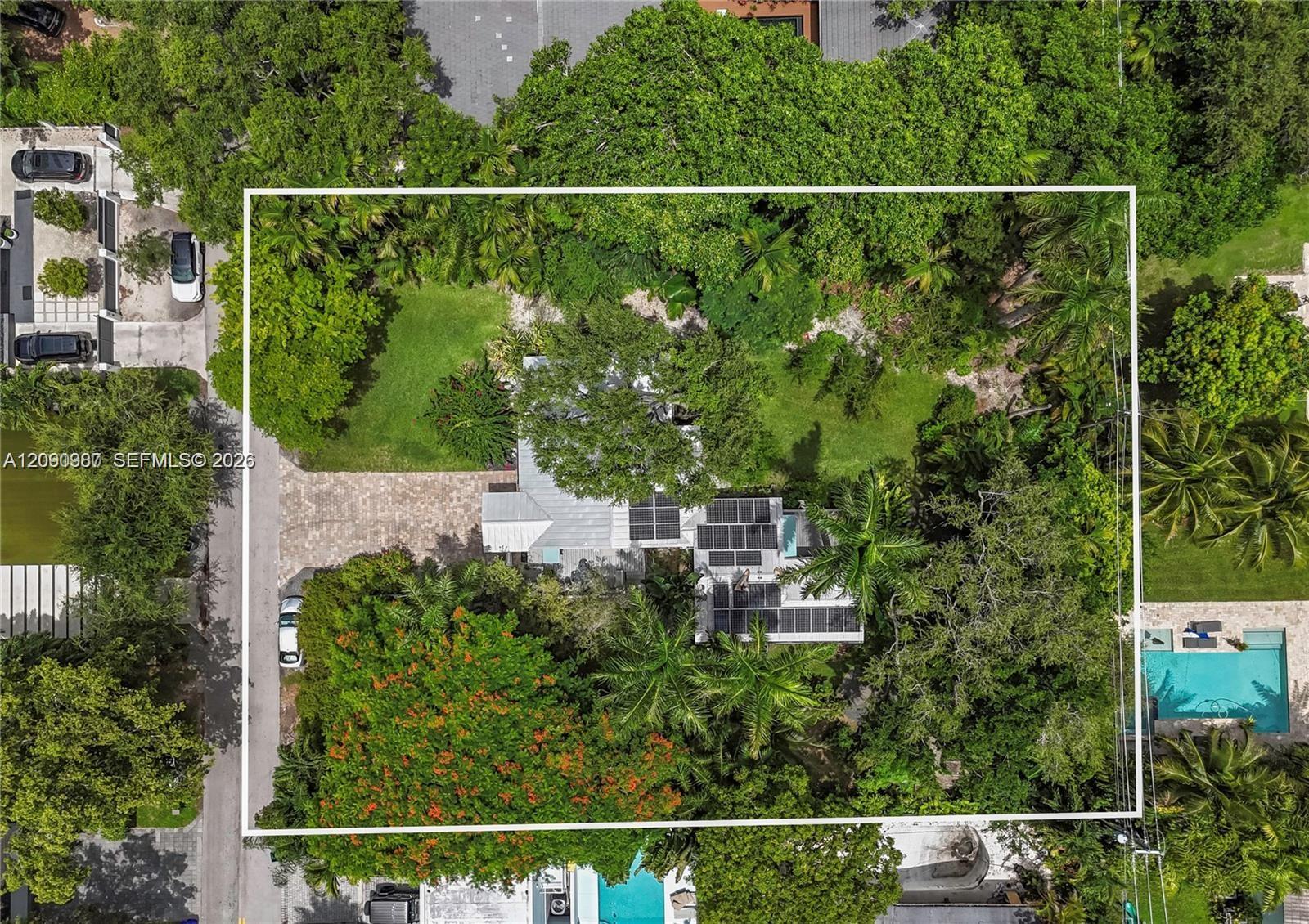 Aerial view of a leafy property outlined in white, with a solar-paneled roof and open lawn.