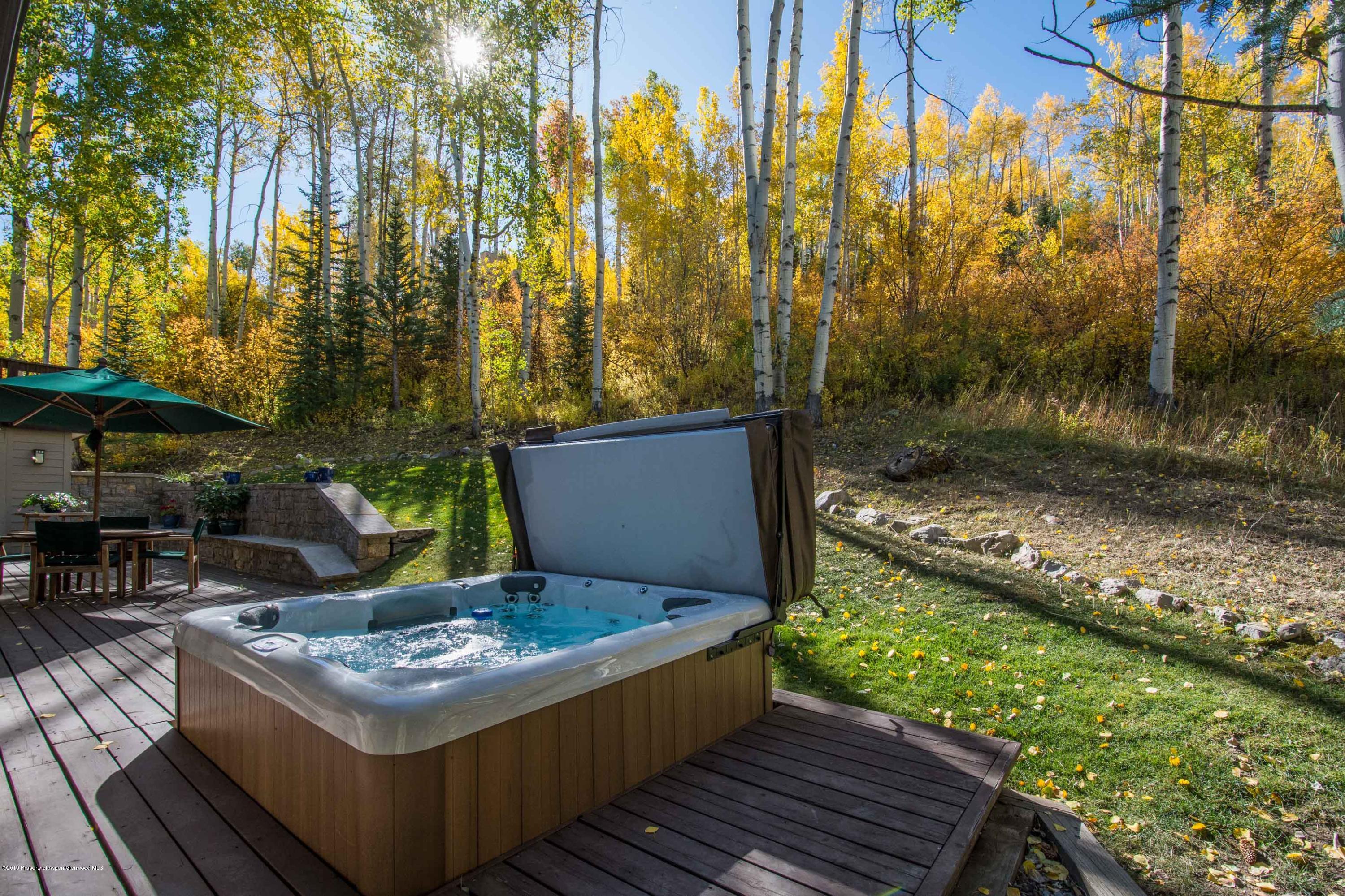 Outdoor hot tub on a deck beside a patio dining area, surrounded by golden autumn aspens.