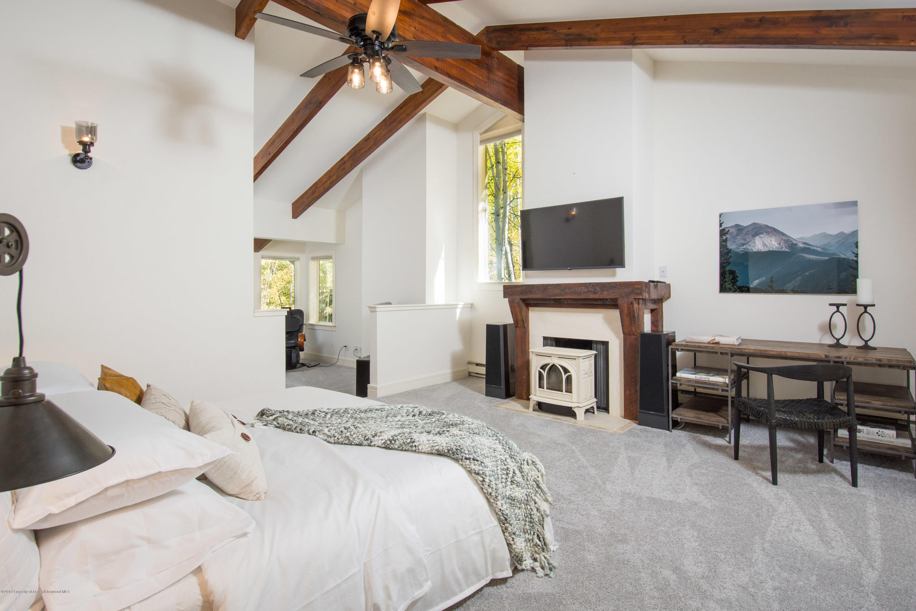 Bedroom with exposed timber beams, a rustic fireplace, and a wall-mounted television.