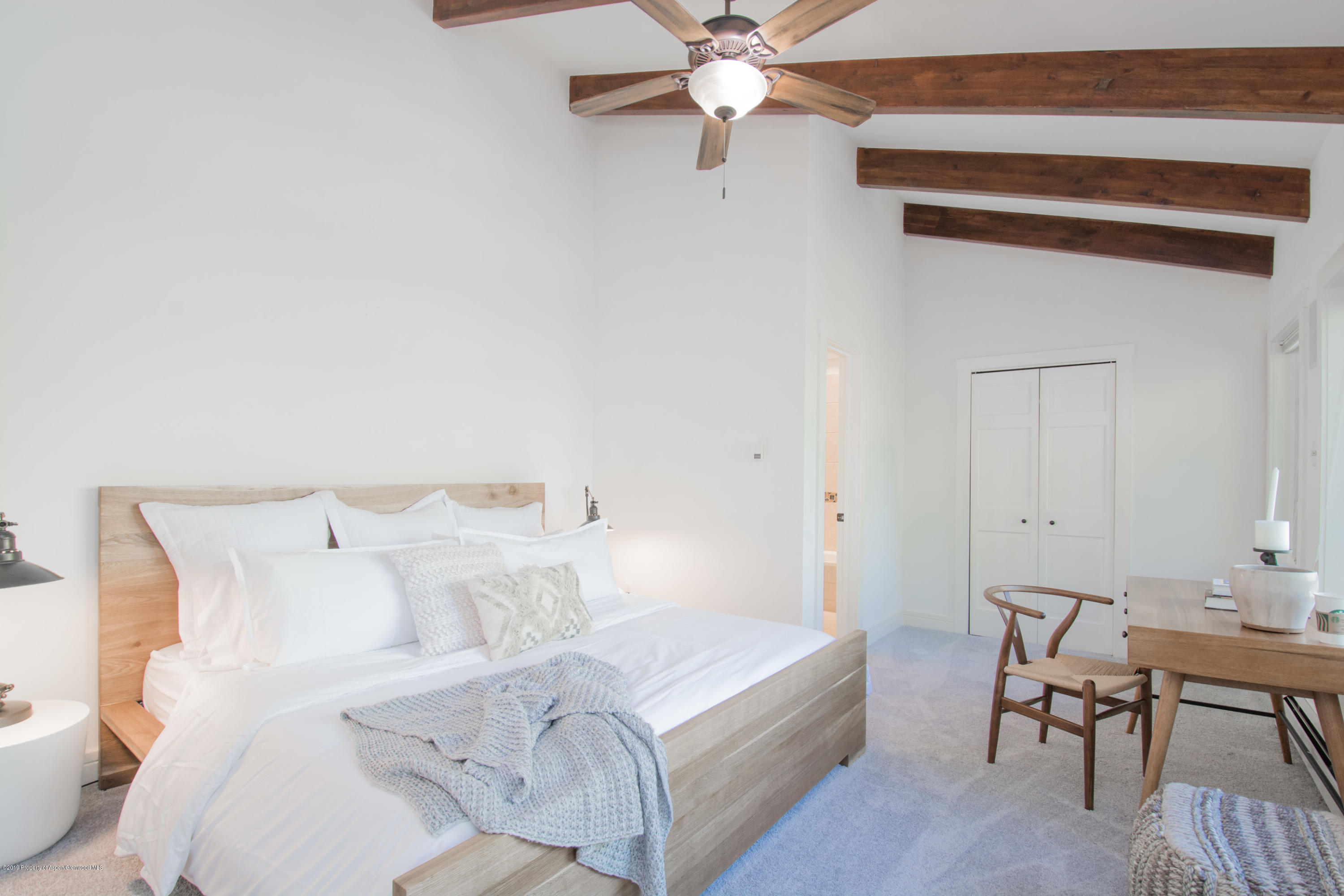 Bedroom with a light wood bed, layered white bedding, exposed ceiling beams, and a desk and chair.