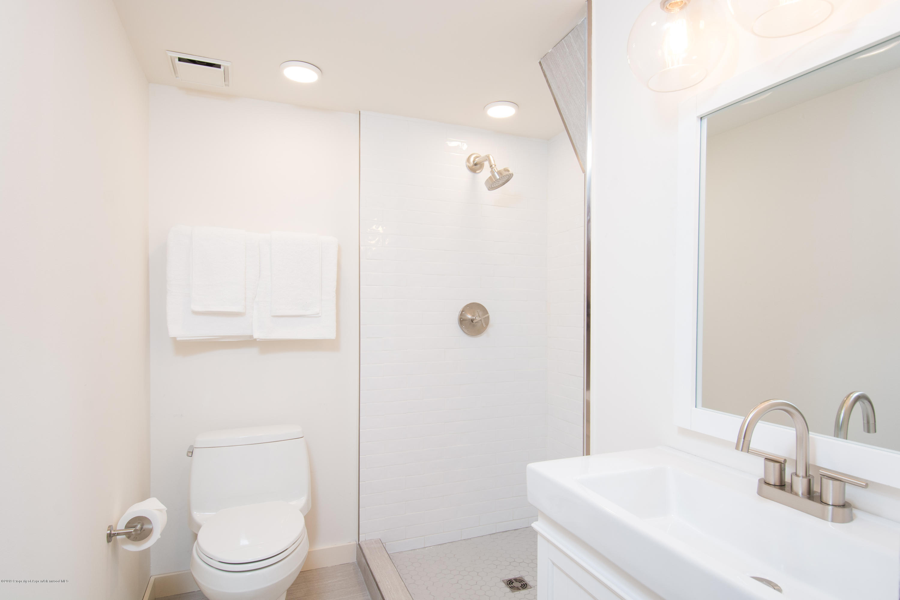 Bright bathroom with a white tiled walk-in shower, chrome fixtures, toilet, and vanity sink.