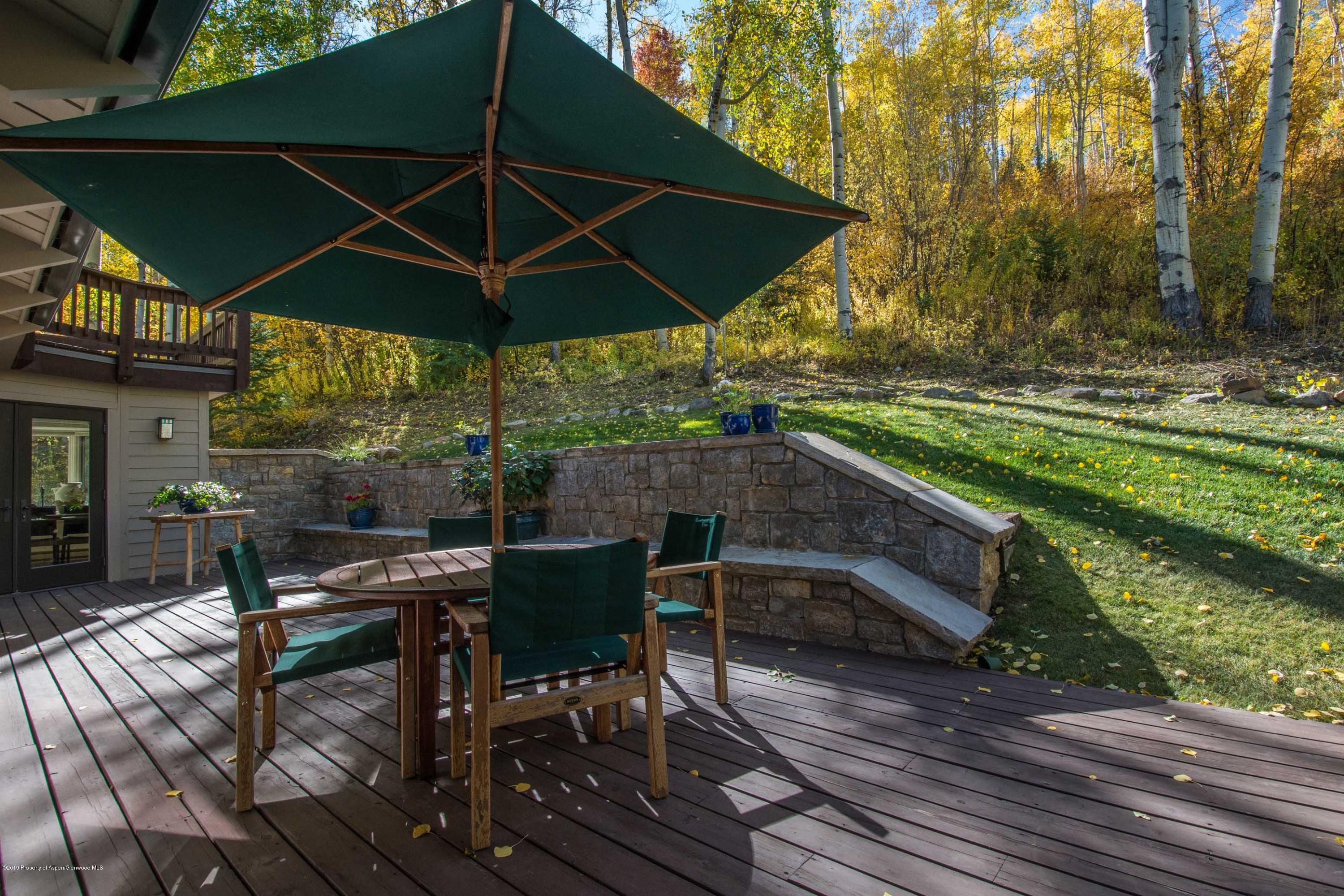 Deck dining area beneath a large umbrella, beside a stone retaining wall and autumn aspens.