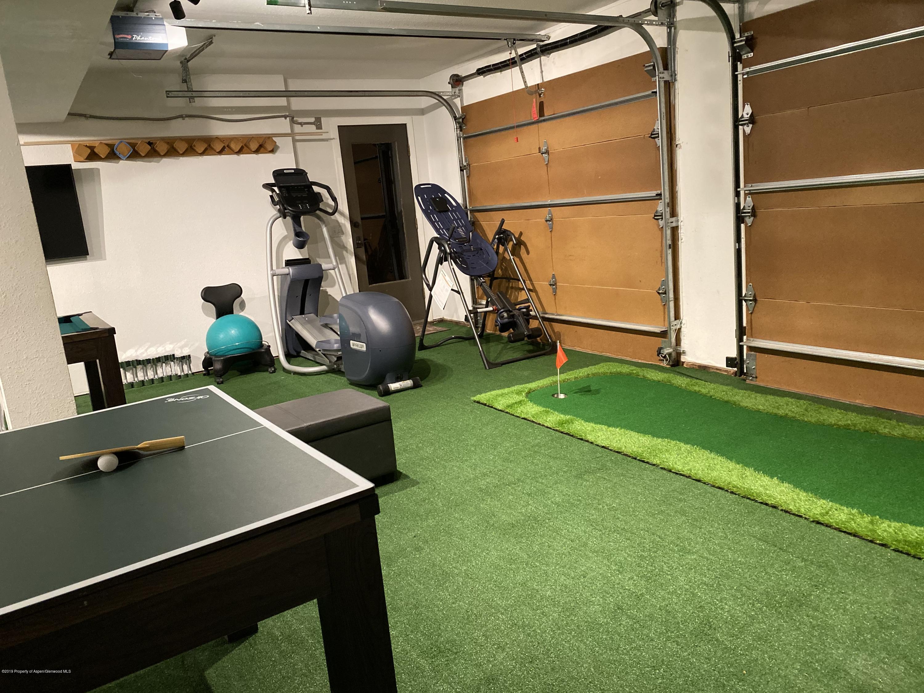 Garage recreation room with a putting green, ping-pong table, and exercise equipment.