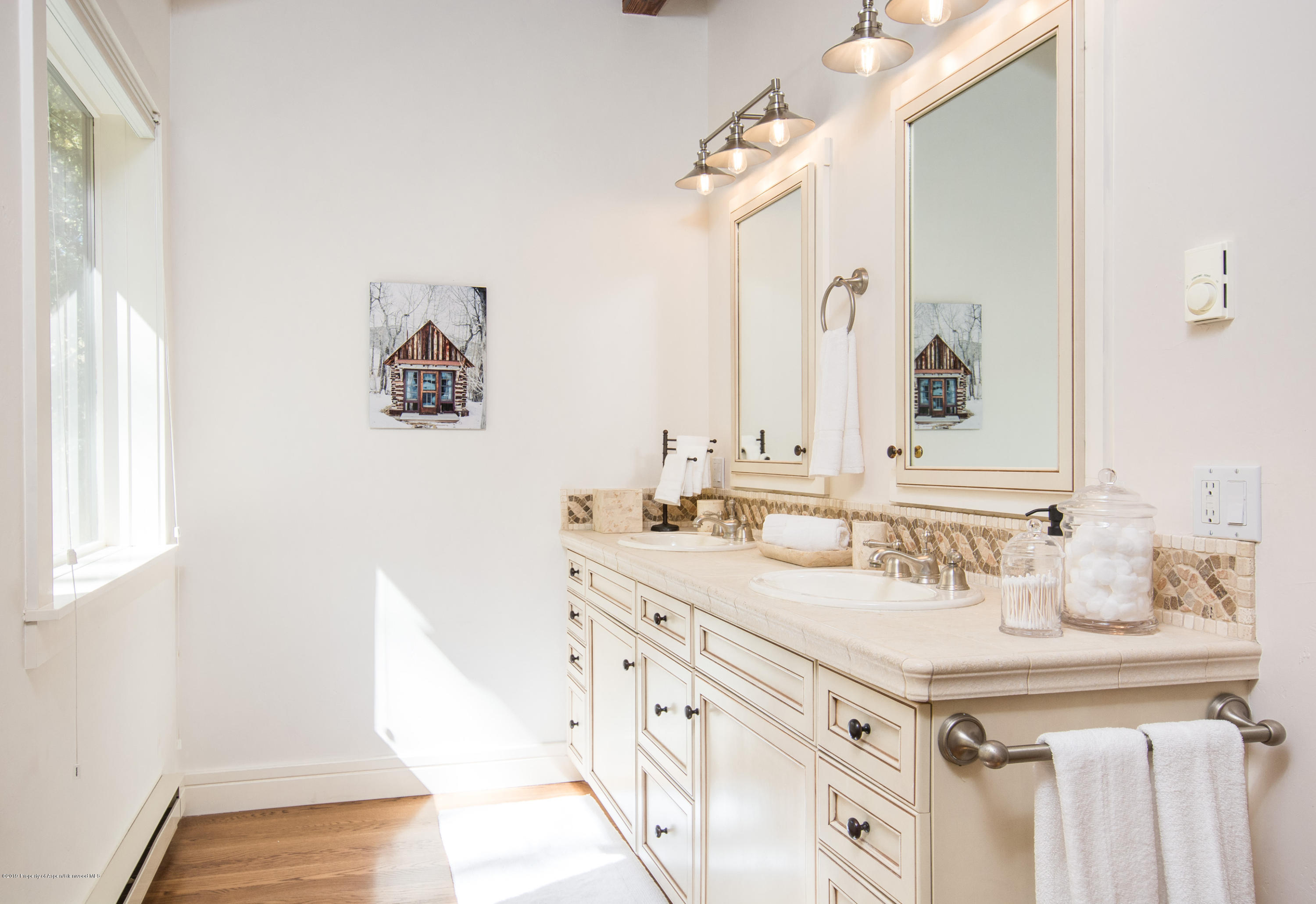Bright bathroom with a cream double vanity, framed mirrors, mosaic backsplash, and sunlit window.