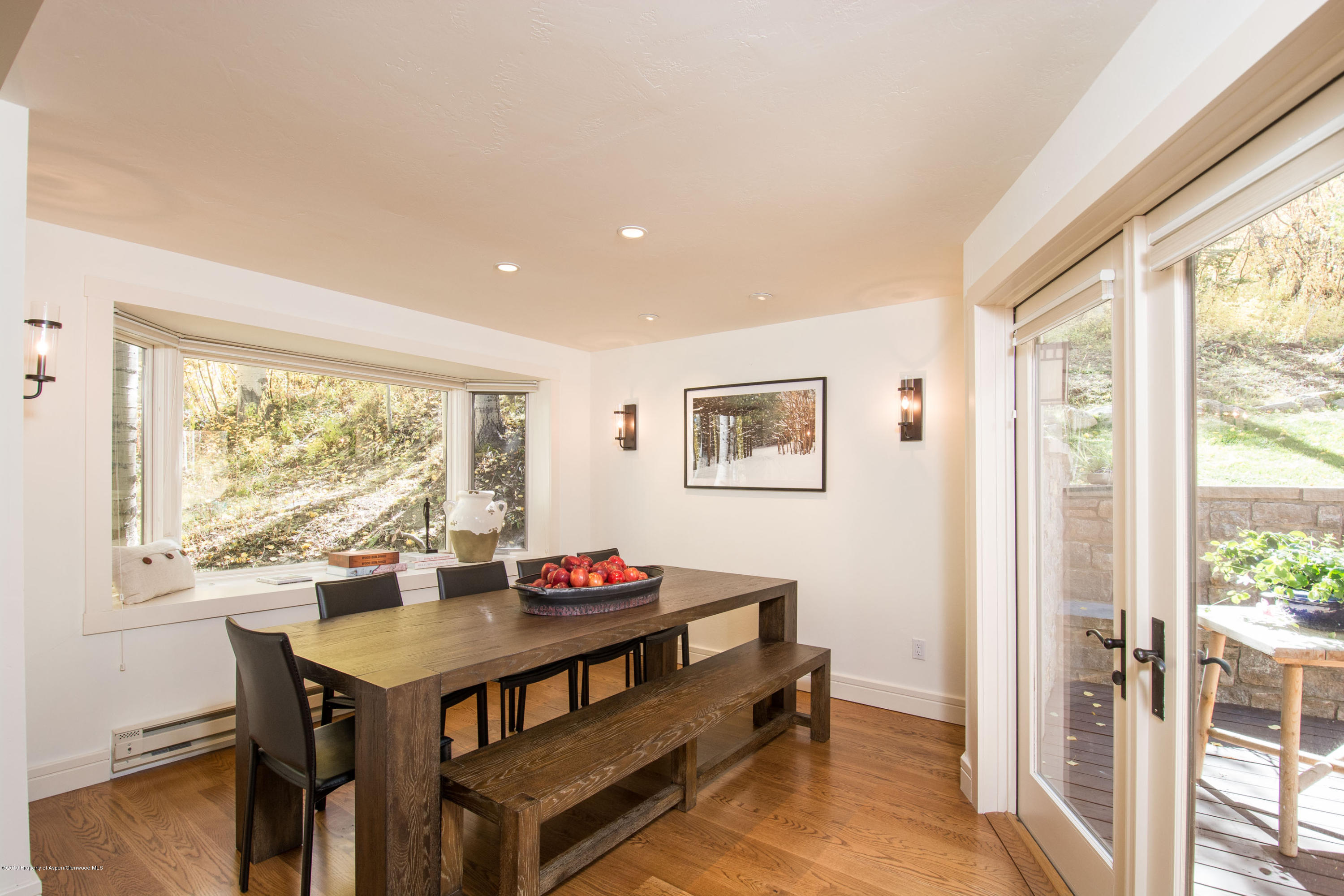 Dining room with a rustic wood table and bench beside wide windows and deck doors.