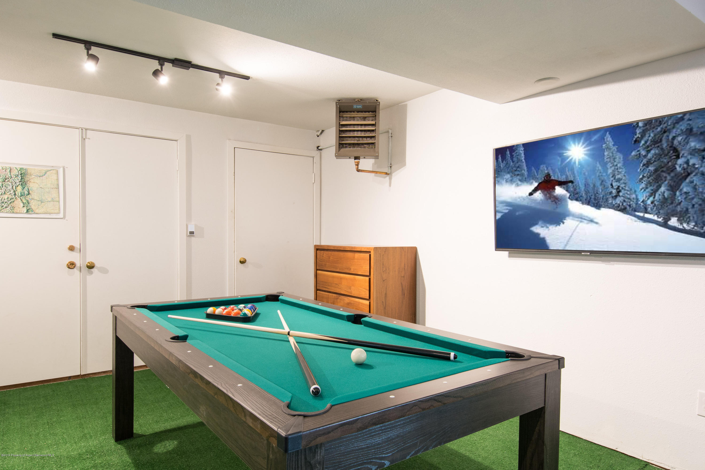Game room with a green-felt pool table, billiard balls and cues, and a television showing a skier.