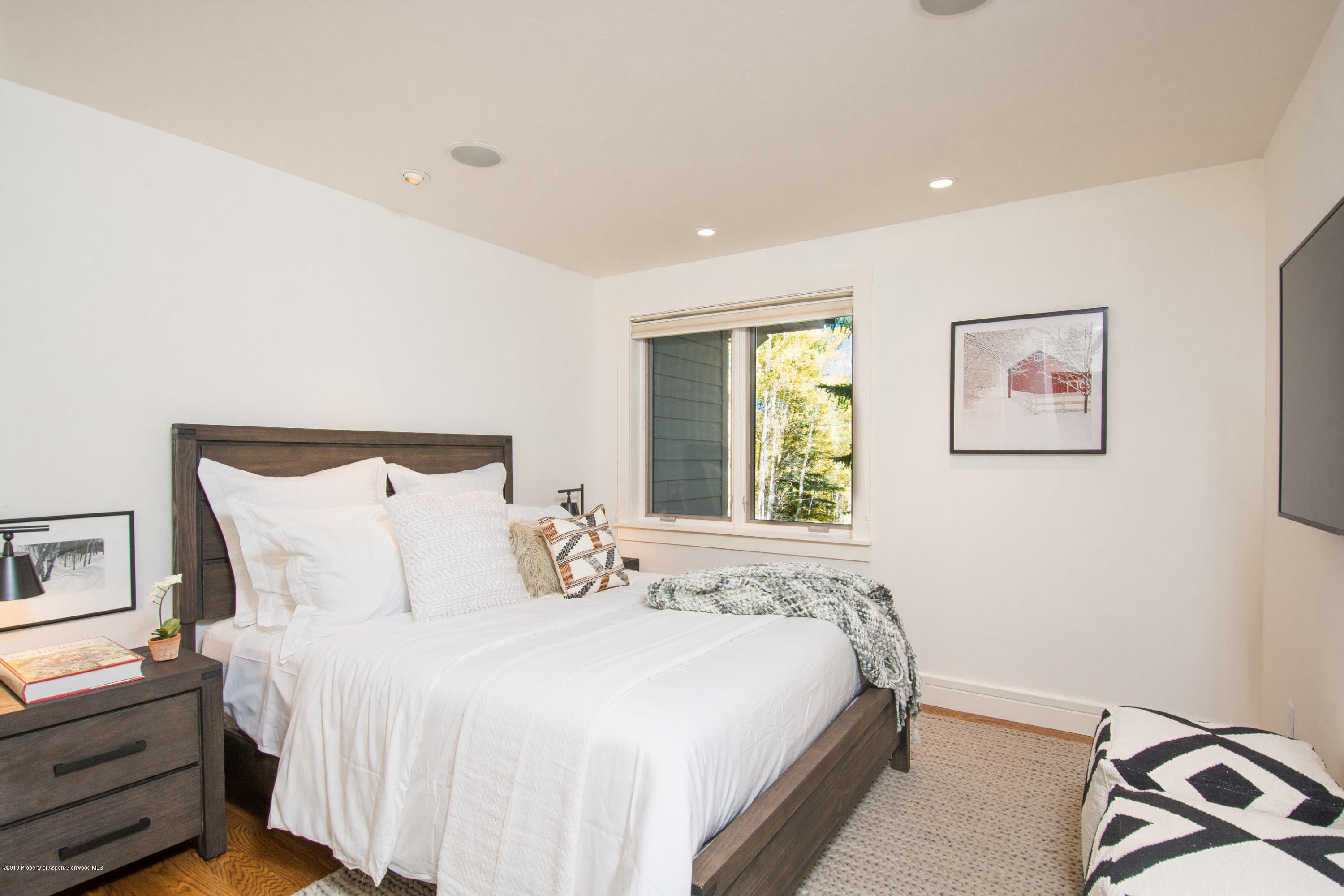 Bedroom with a dark wood bed, crisp white bedding, and a window overlooking leafy trees.