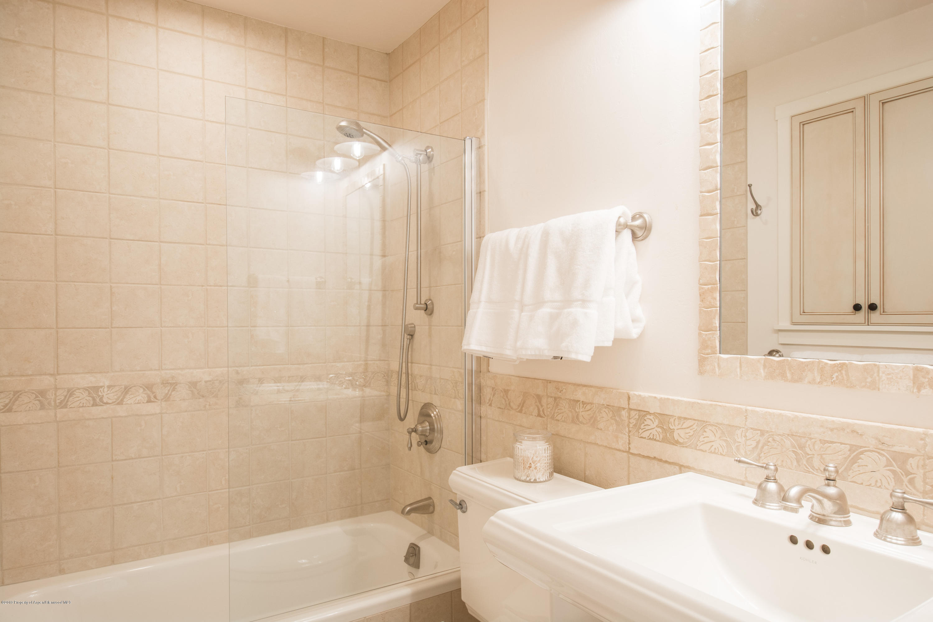 Bathroom with a tiled tub and glass shower, white vanity, and folded towels.