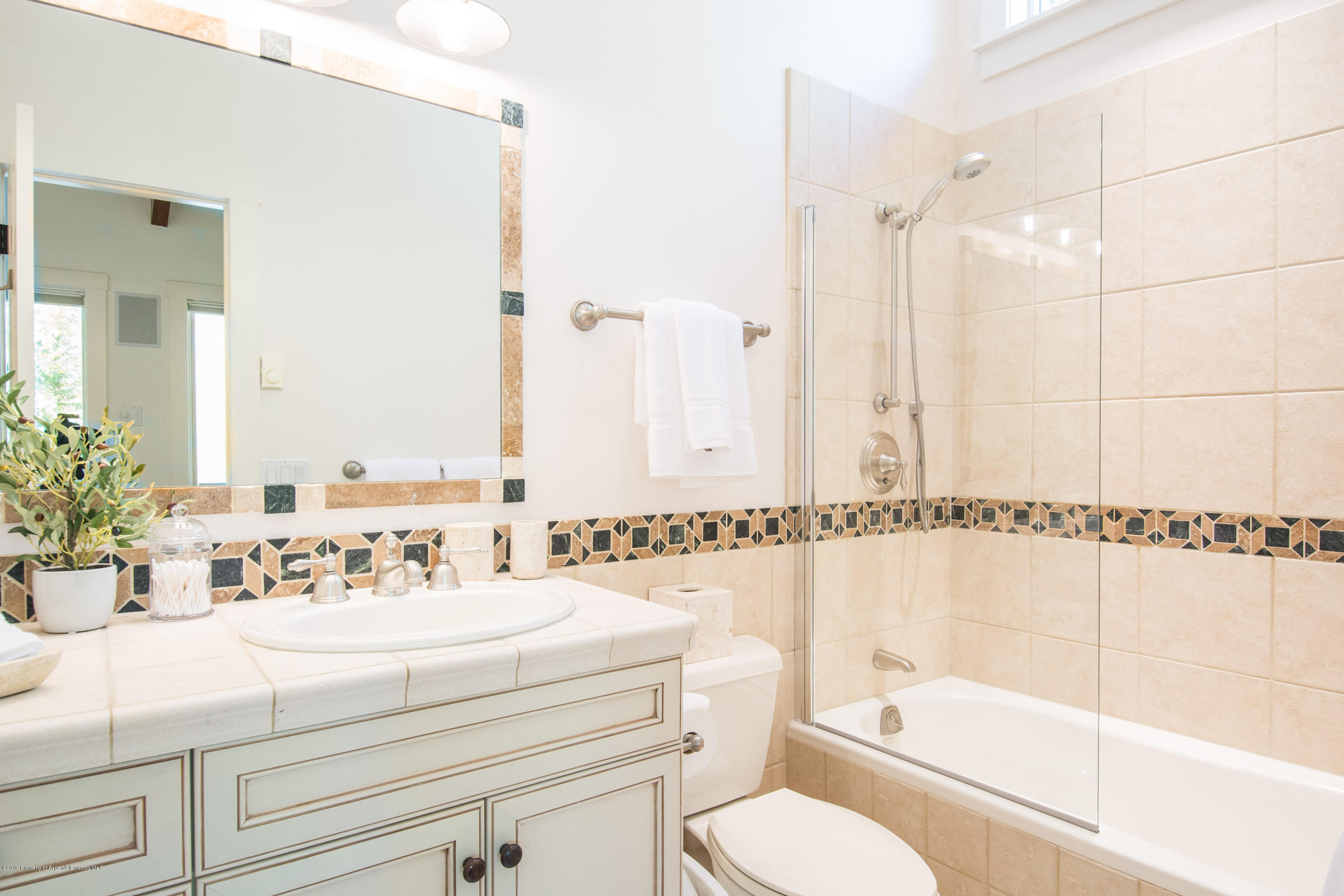 Bathroom with a tiled vanity and mirror beside a bathtub with a glass shower screen.