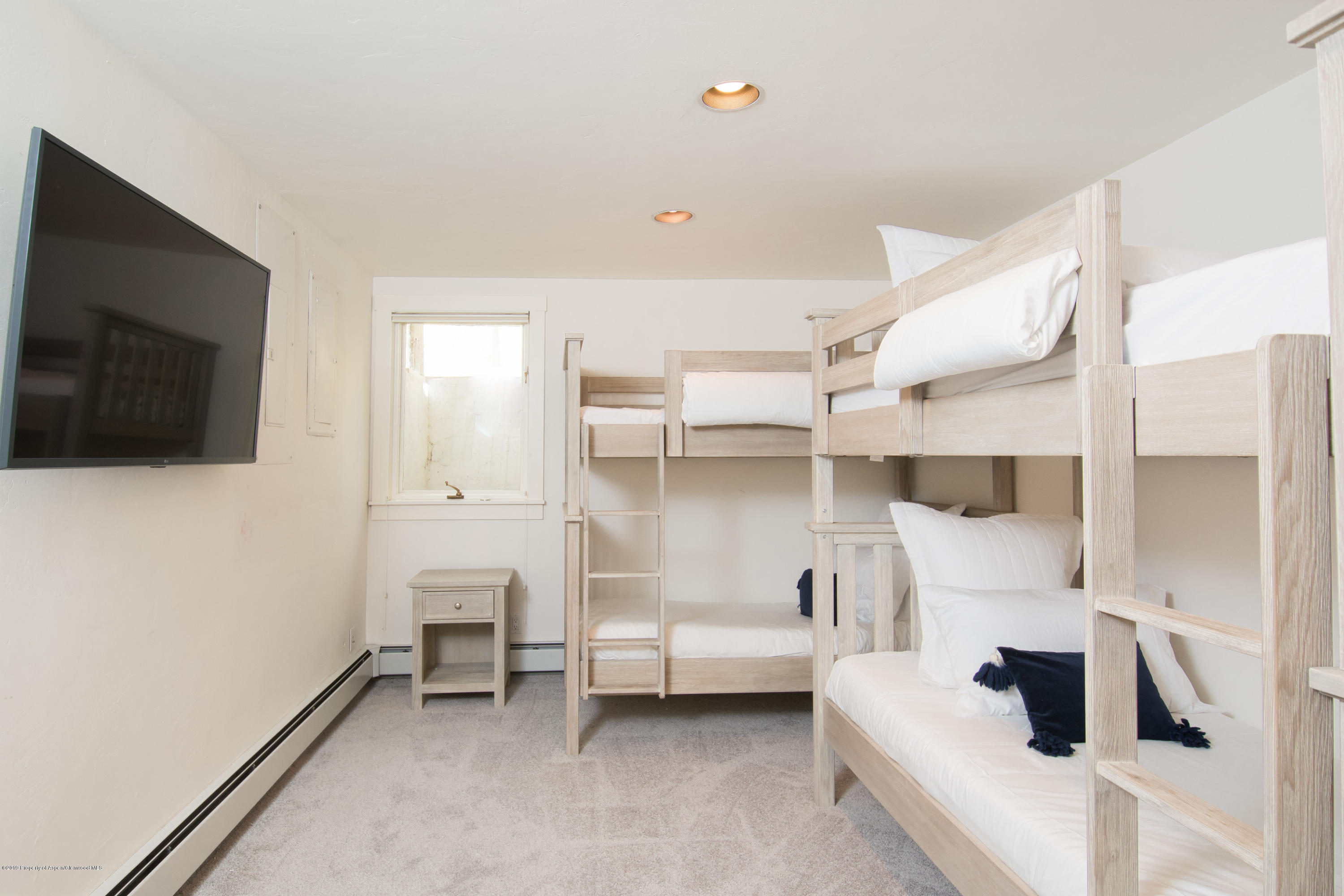 Bedroom with light wood bunk beds, white bedding, and a wall-mounted television.