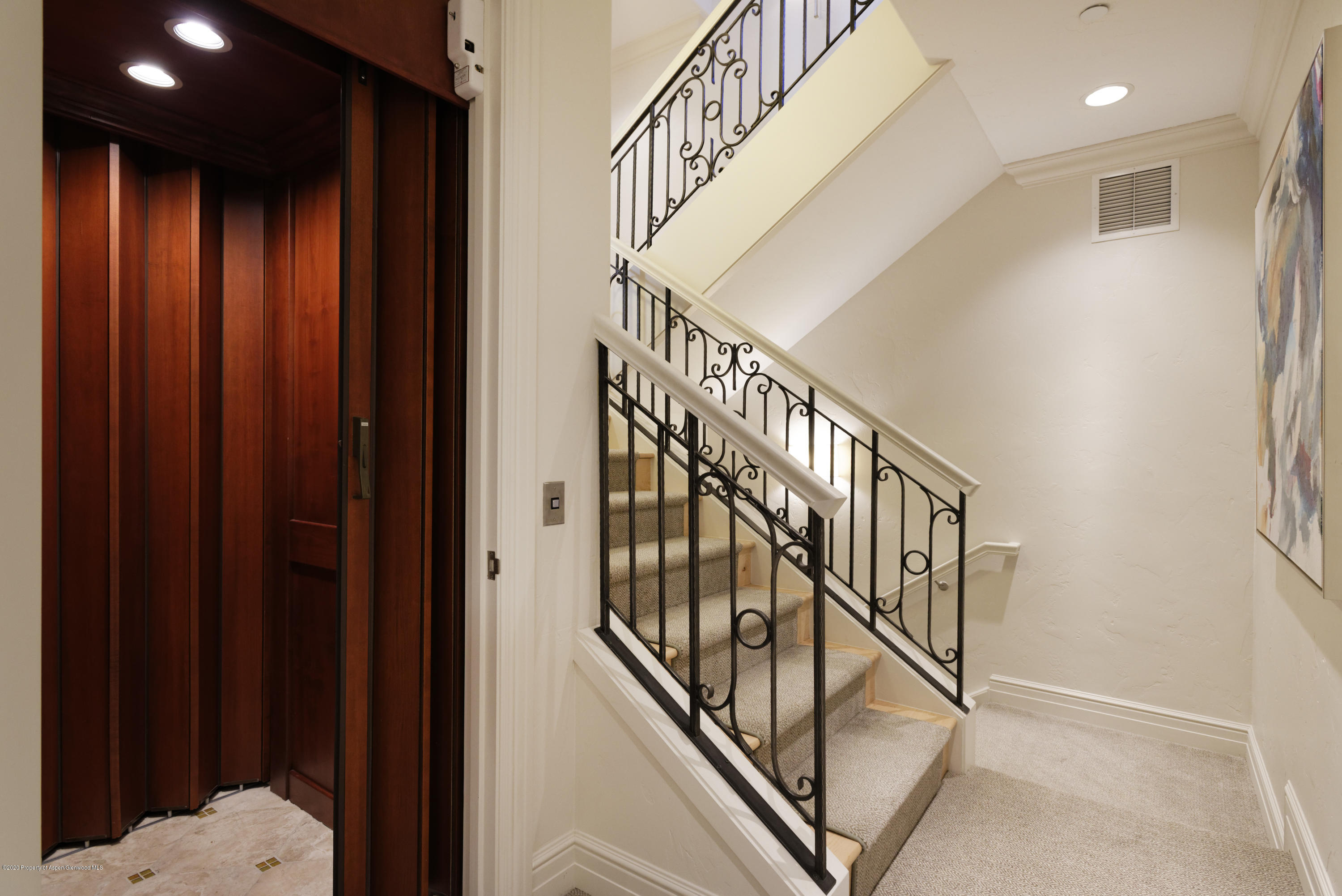 Carpeted staircase with ornate iron railings beside a dark wood-paneled elevator.