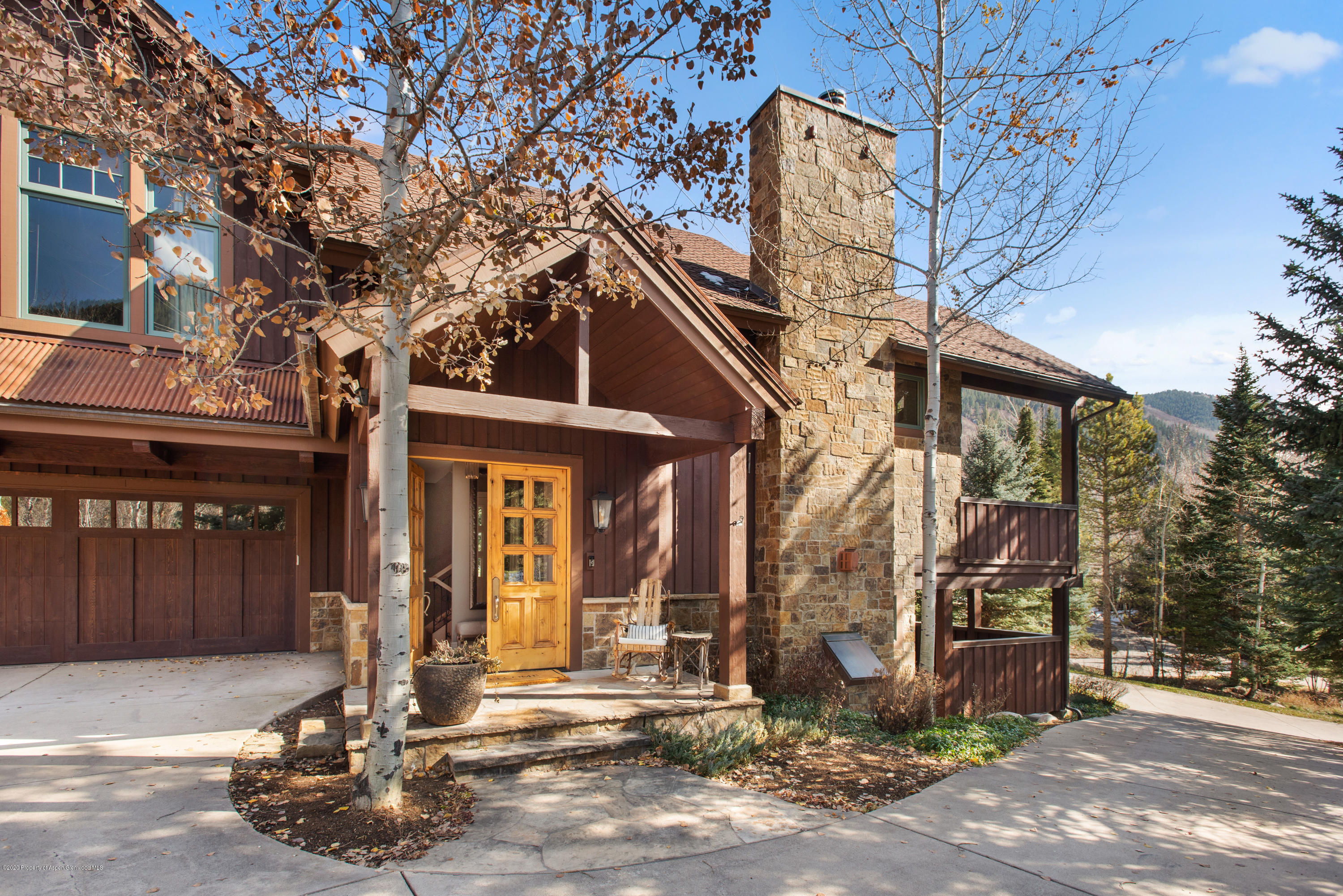 Mountain-style home with a stone chimney, golden entry door, and autumn aspen trees.