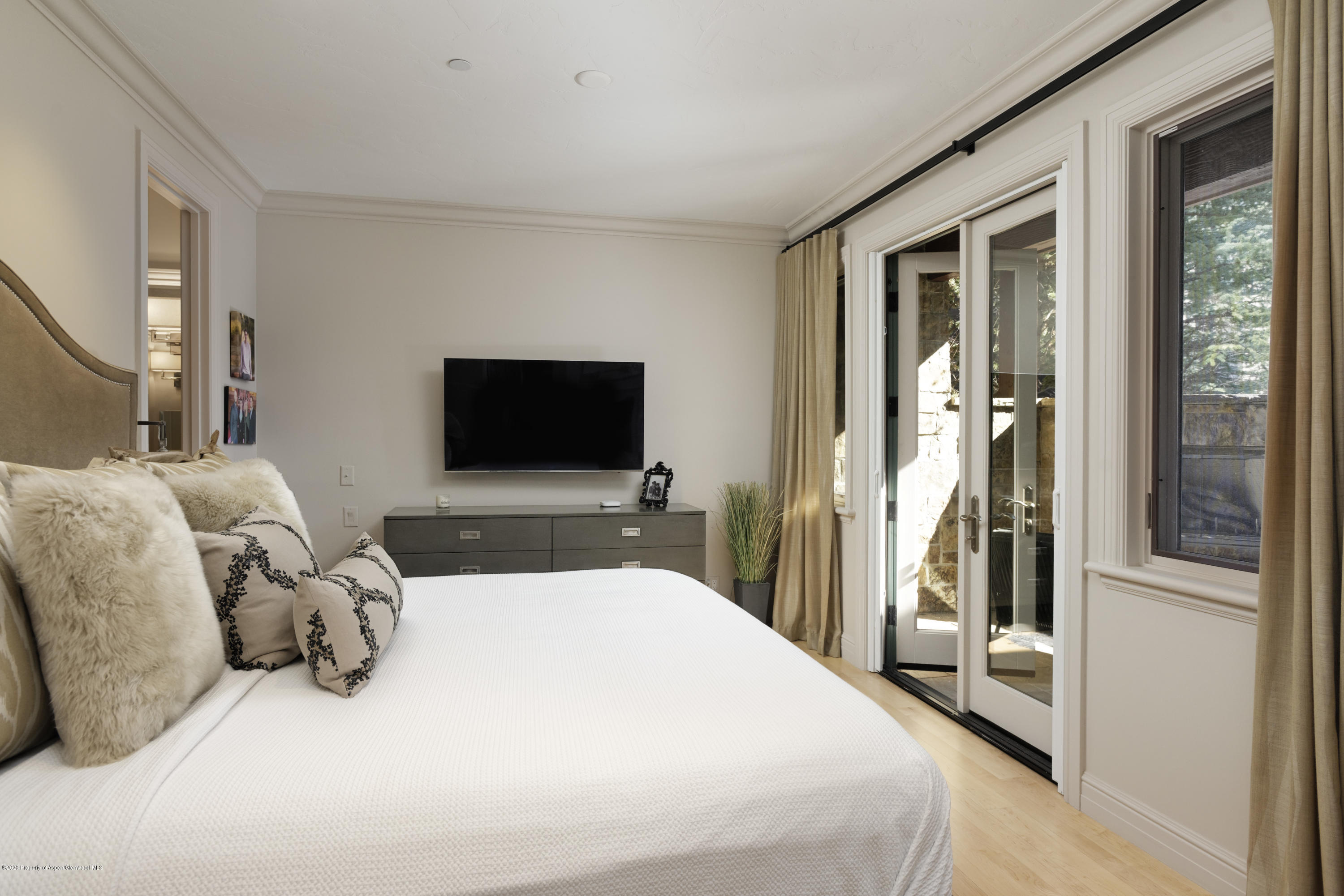 Bedroom with a white bed, wall-mounted television, and glass doors opening to a stone patio.