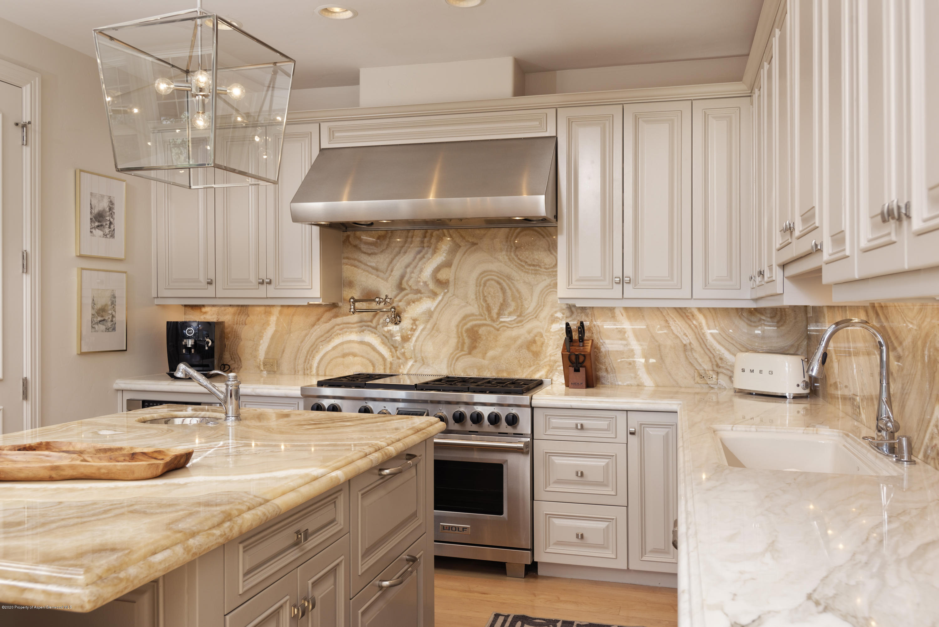 Upscale kitchen with a Wolf range, golden veined stone counters, white cabinetry, and a large island.