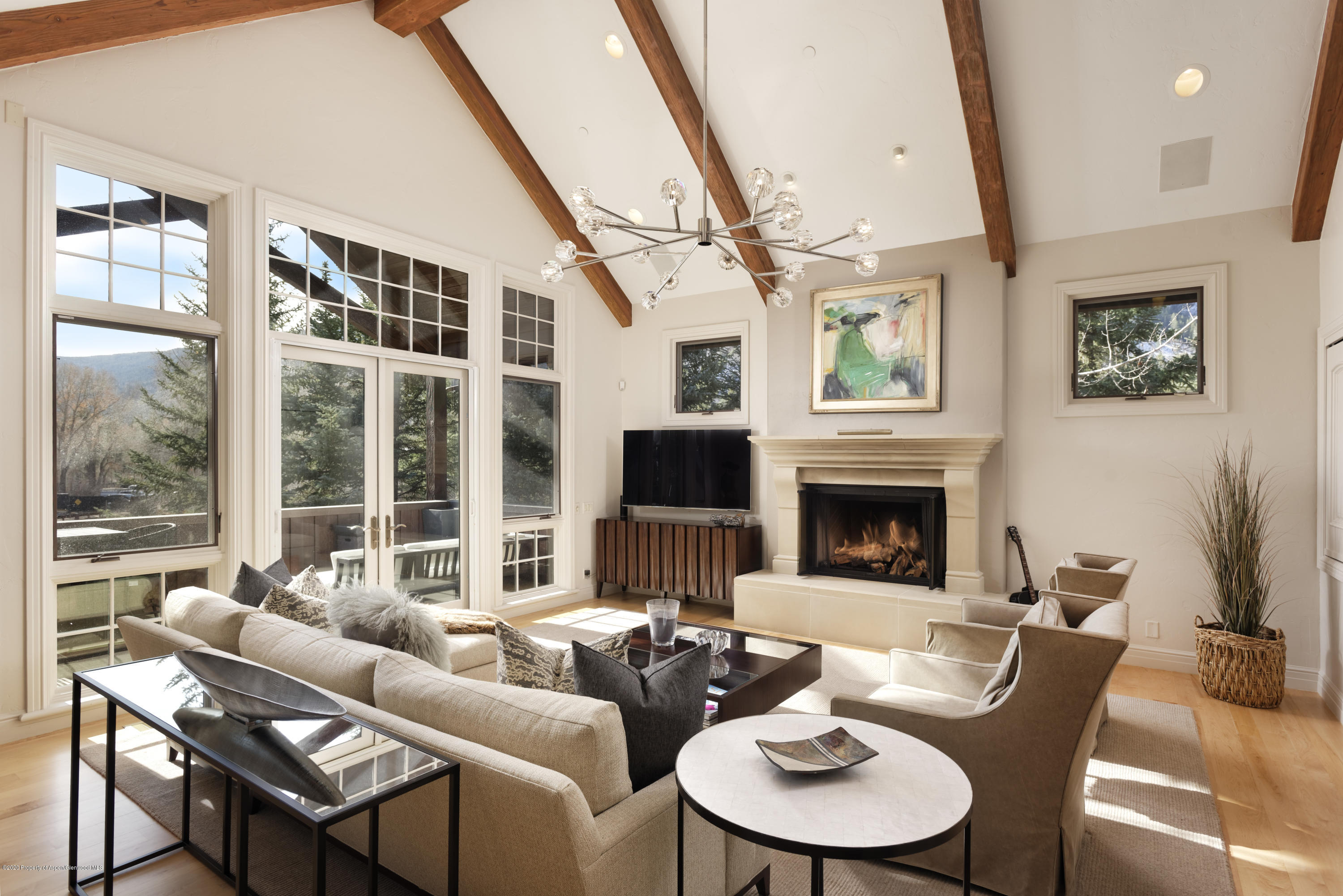 Living room with vaulted wood-beam ceiling, fireplace, and large windows overlooking trees and mountains.