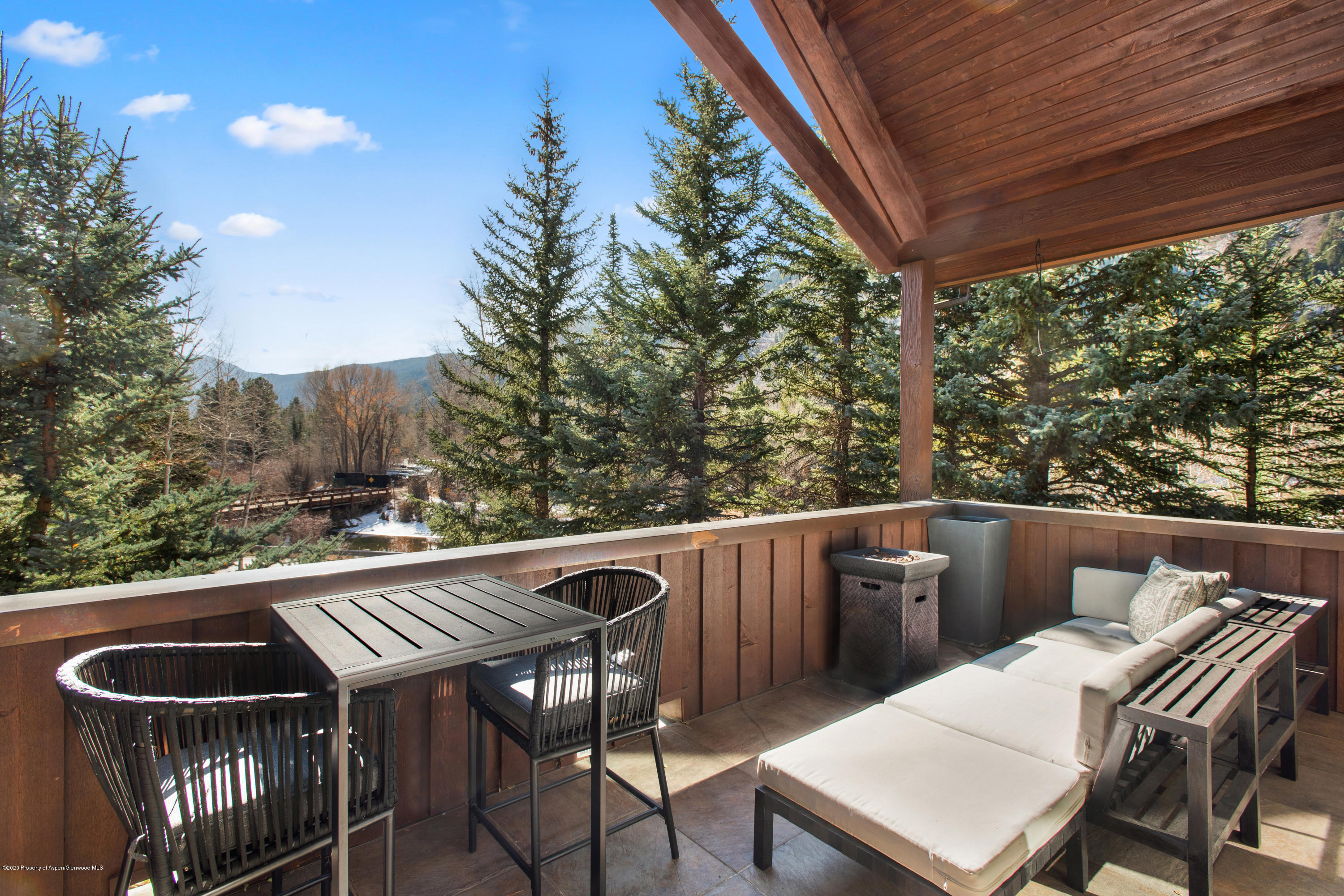 Covered deck with dining and lounge seating overlooking evergreen trees and a mountain.