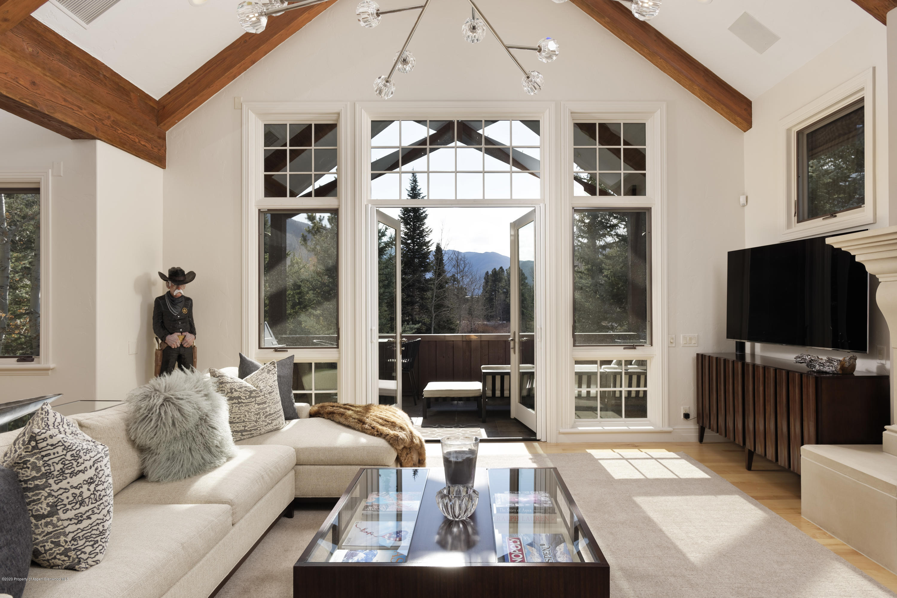 Living room with exposed timber beams, a vaulted ceiling, and balcony doors framing a mountain view.