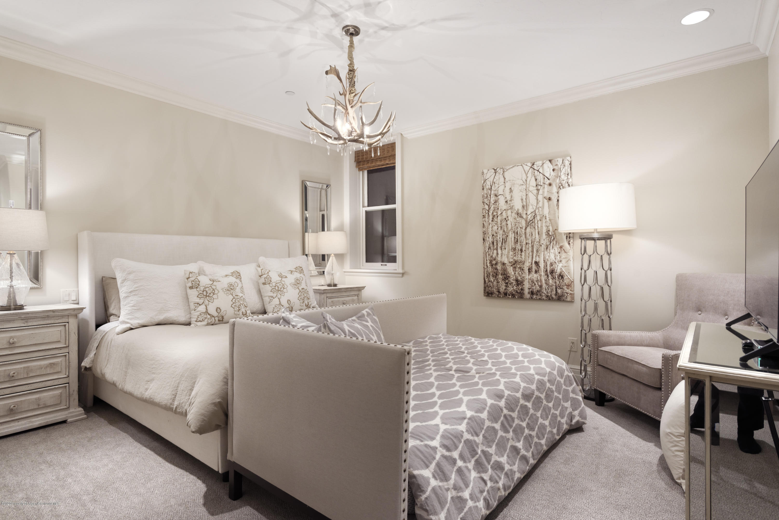 Furnished bedroom with an upholstered bed, patterned duvet, and antler chandelier.