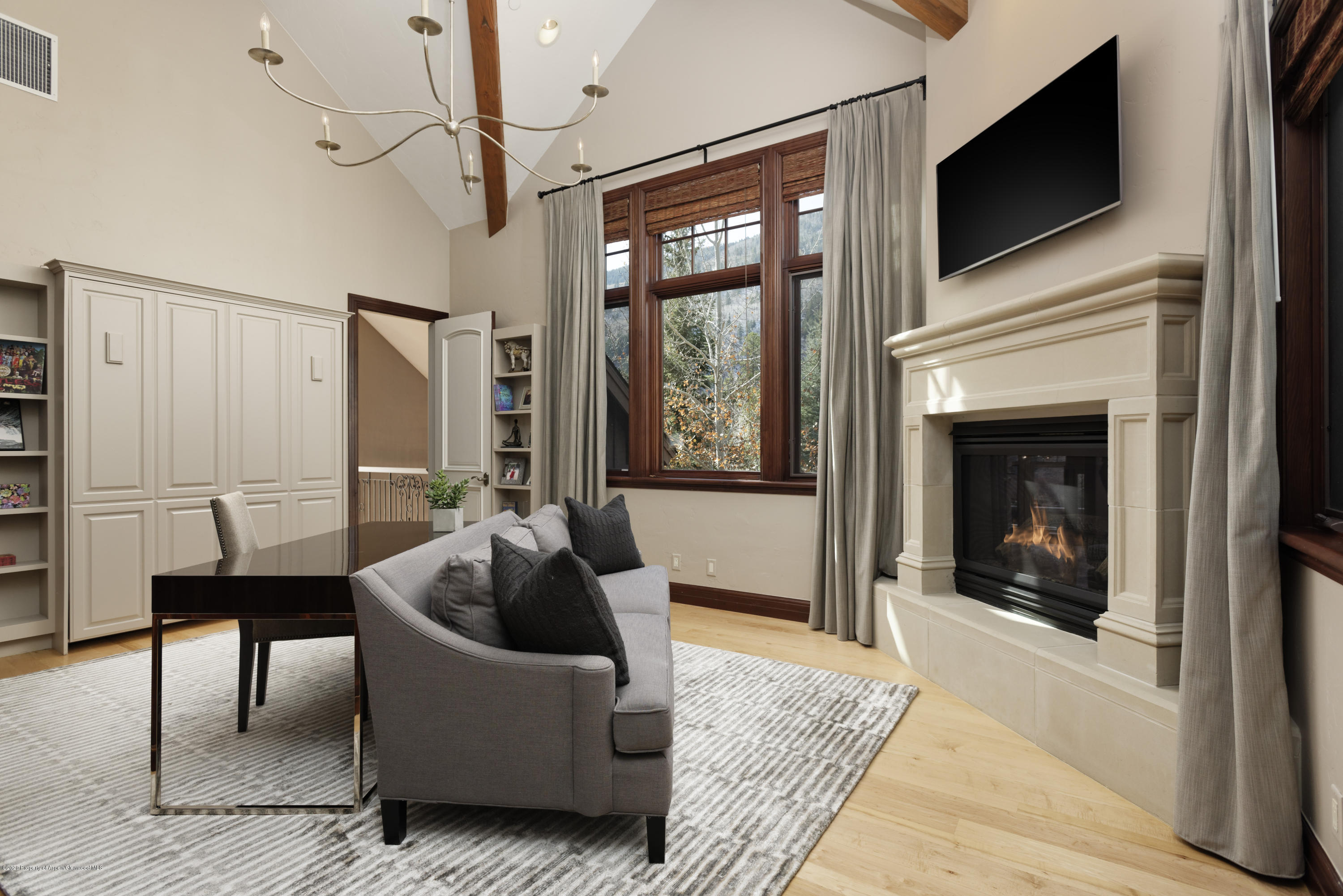 Living room with a fireplace, gray sofa, and tall windows overlooking trees and a mountain.