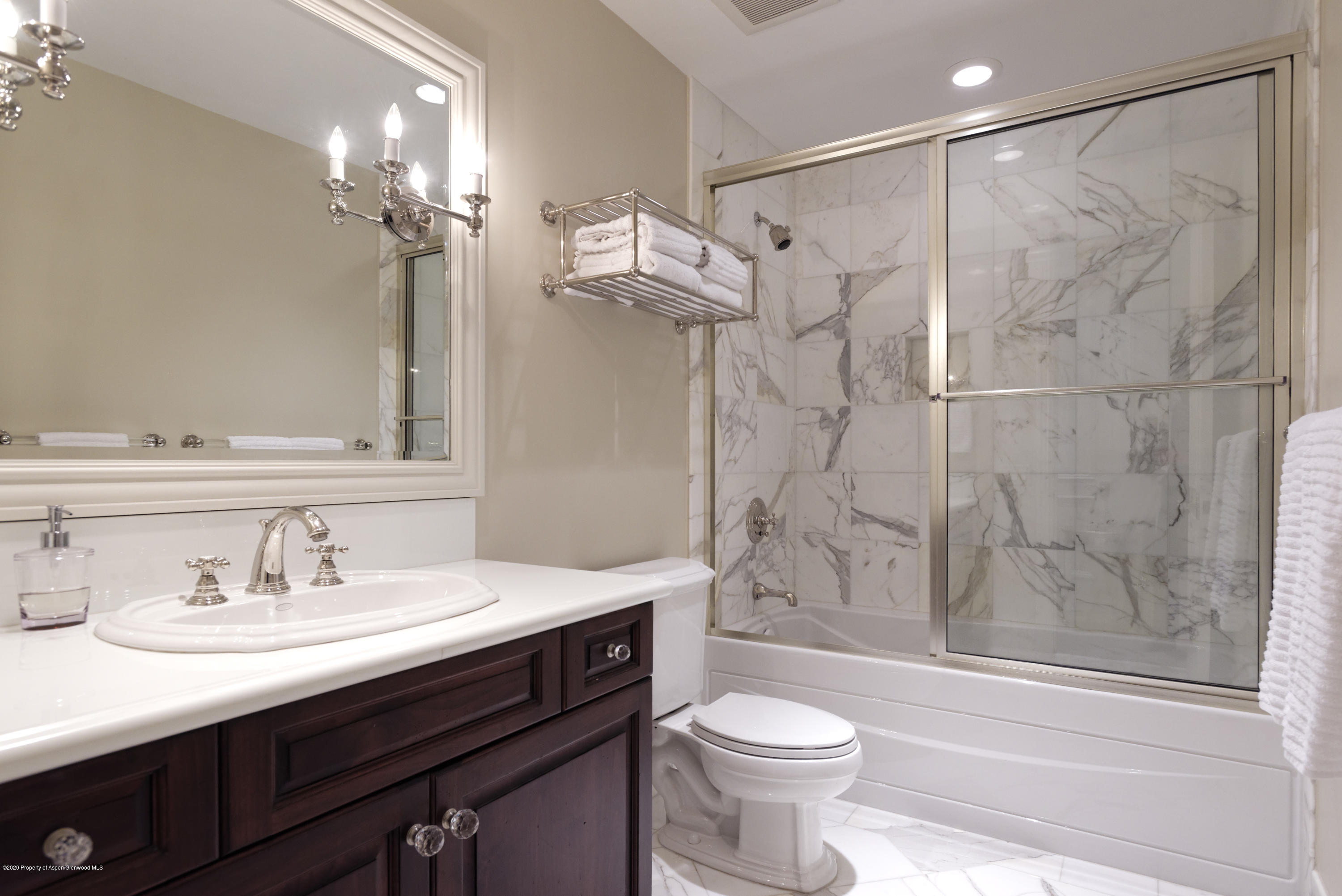 Bathroom with a dark wood vanity and a marble-tiled tub and shower behind glass doors.