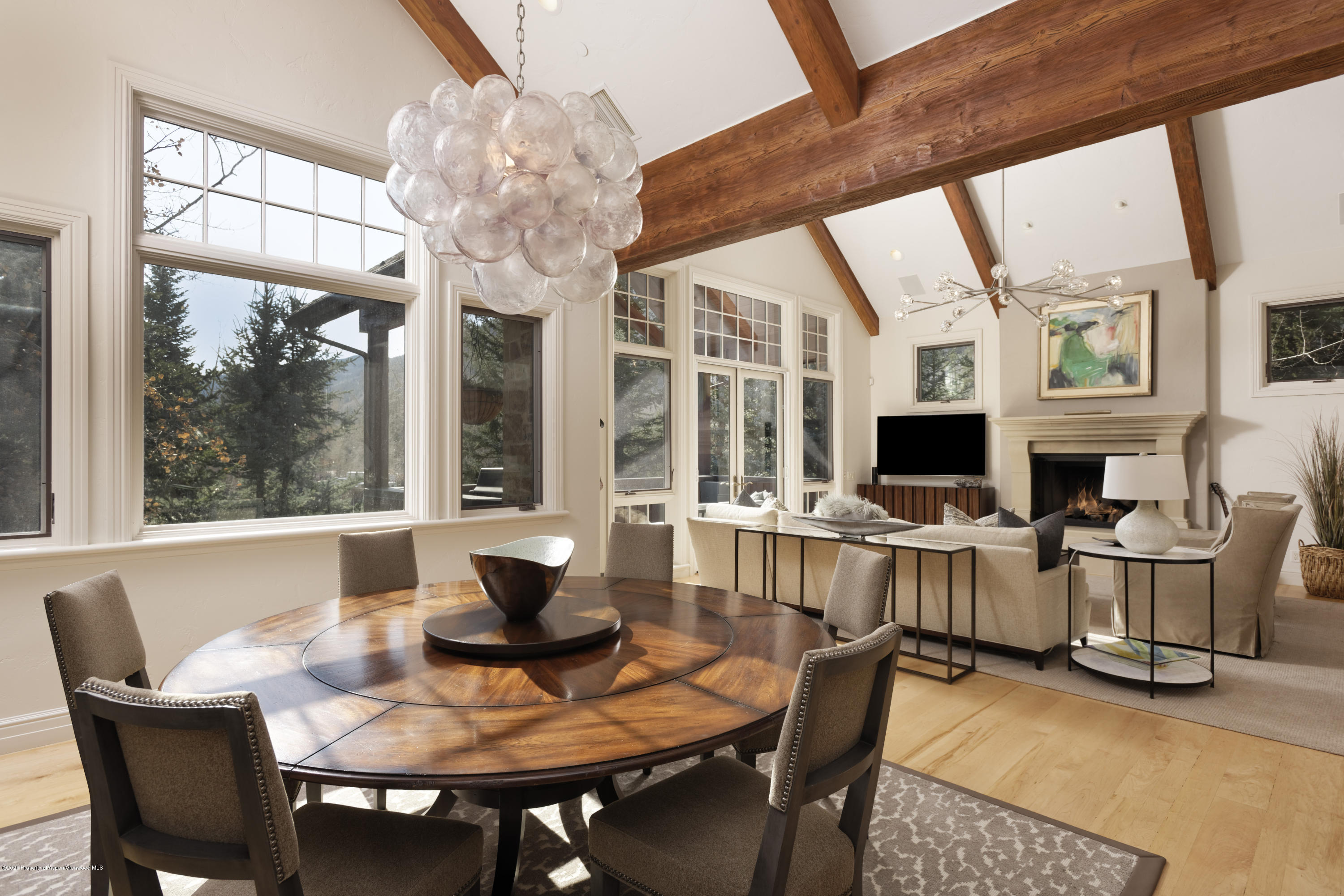 Open-plan dining and living room with exposed beams, large windows, and a fireplace.