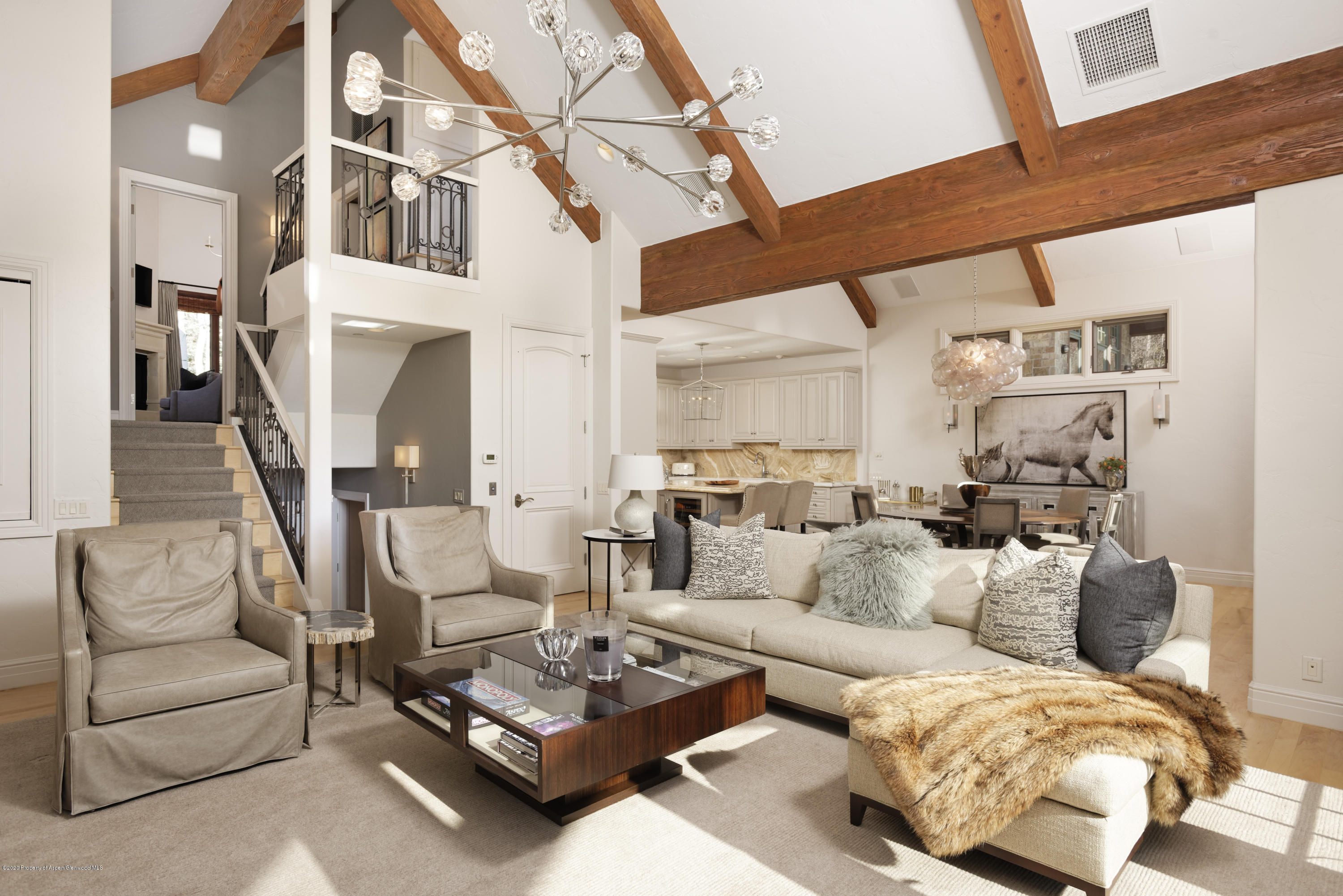 Living room with vaulted ceilings, exposed timber beams, and a staircase opening to the kitchen and dining area.