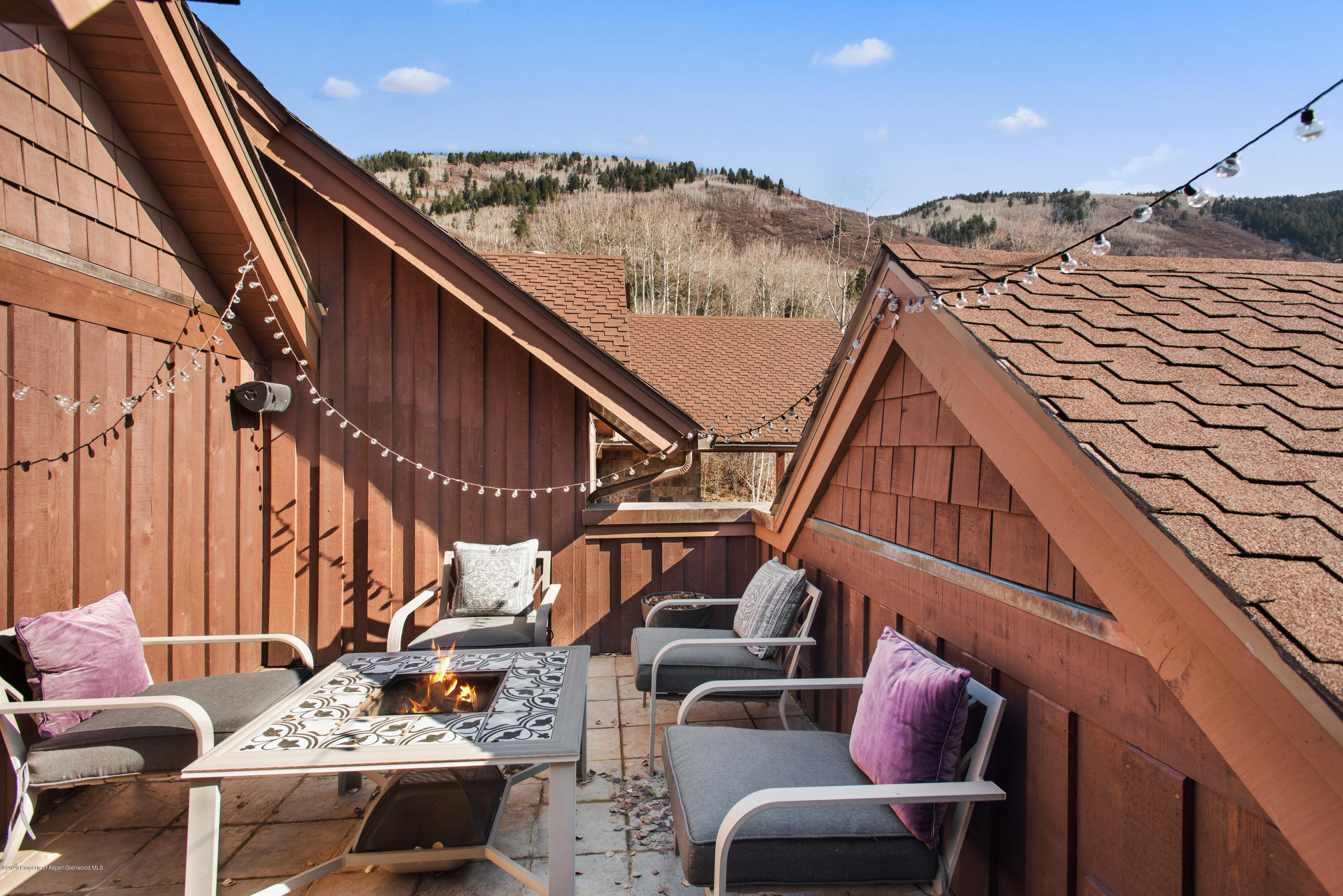 Rooftop deck with lounge chairs, string lights, a lit fire table, and wooded mountain views.