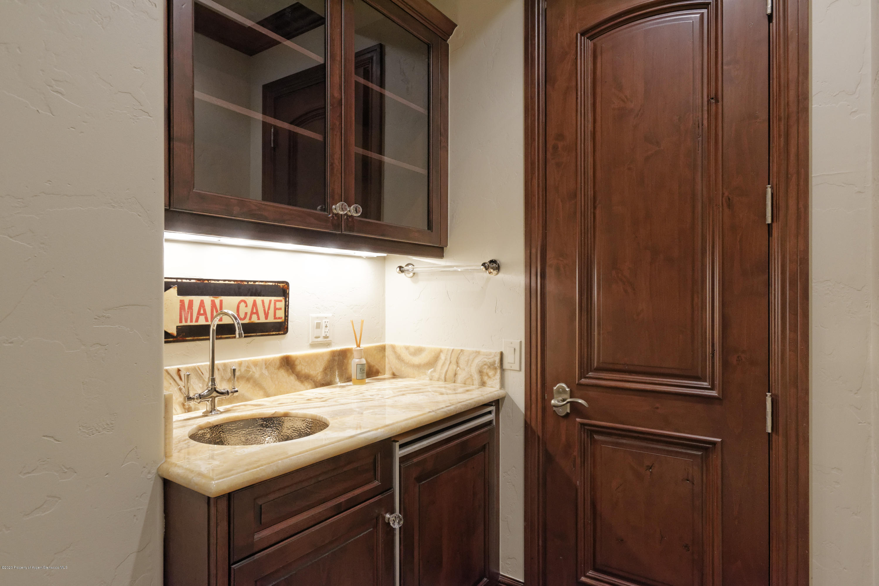 Bathroom vanity with a marble counter, hammered-metal sink, dark wood cabinetry, and a “MAN CAVE” sign.