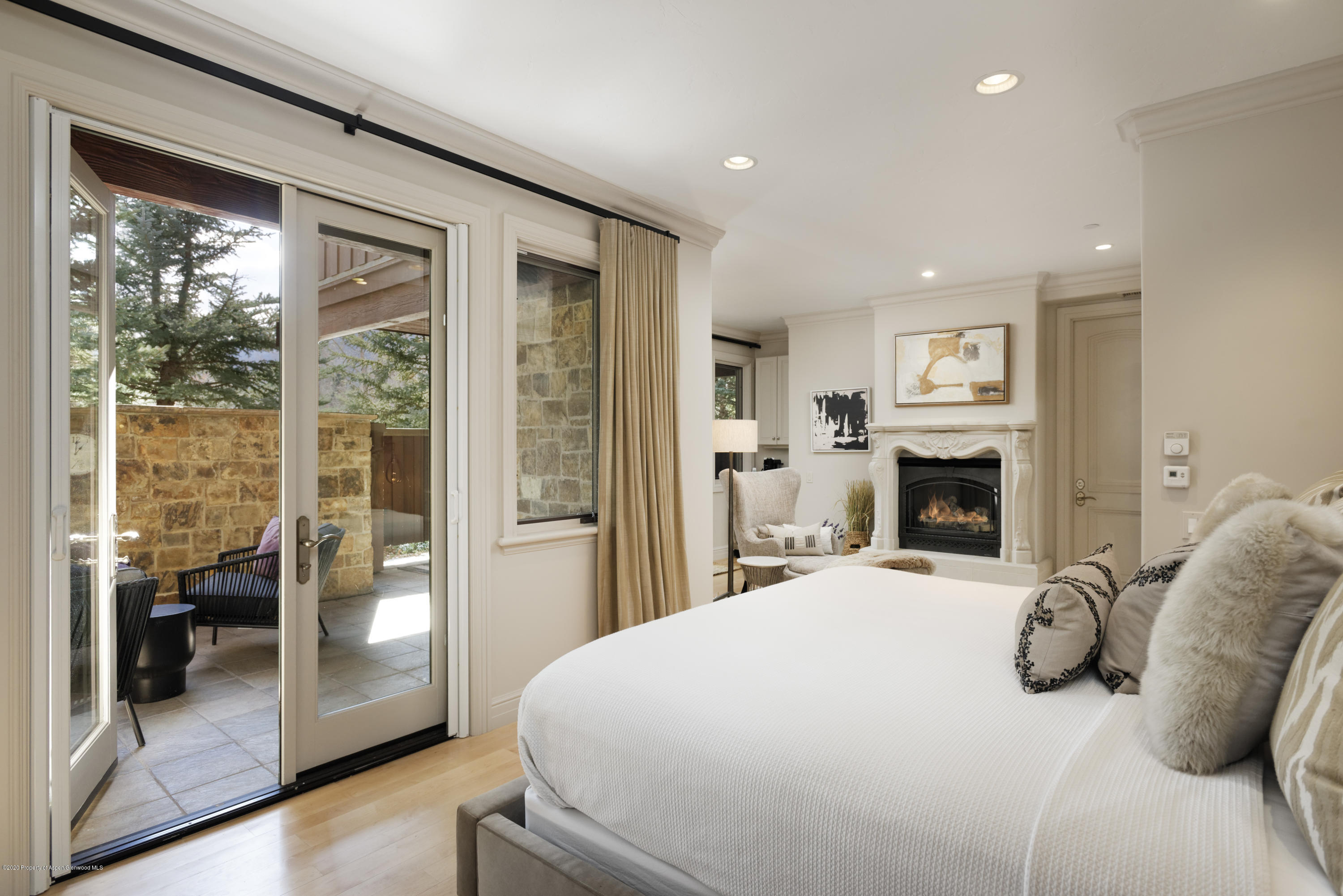 Furnished bedroom with a white bed, ornate fireplace, and sliding doors to a stone patio.