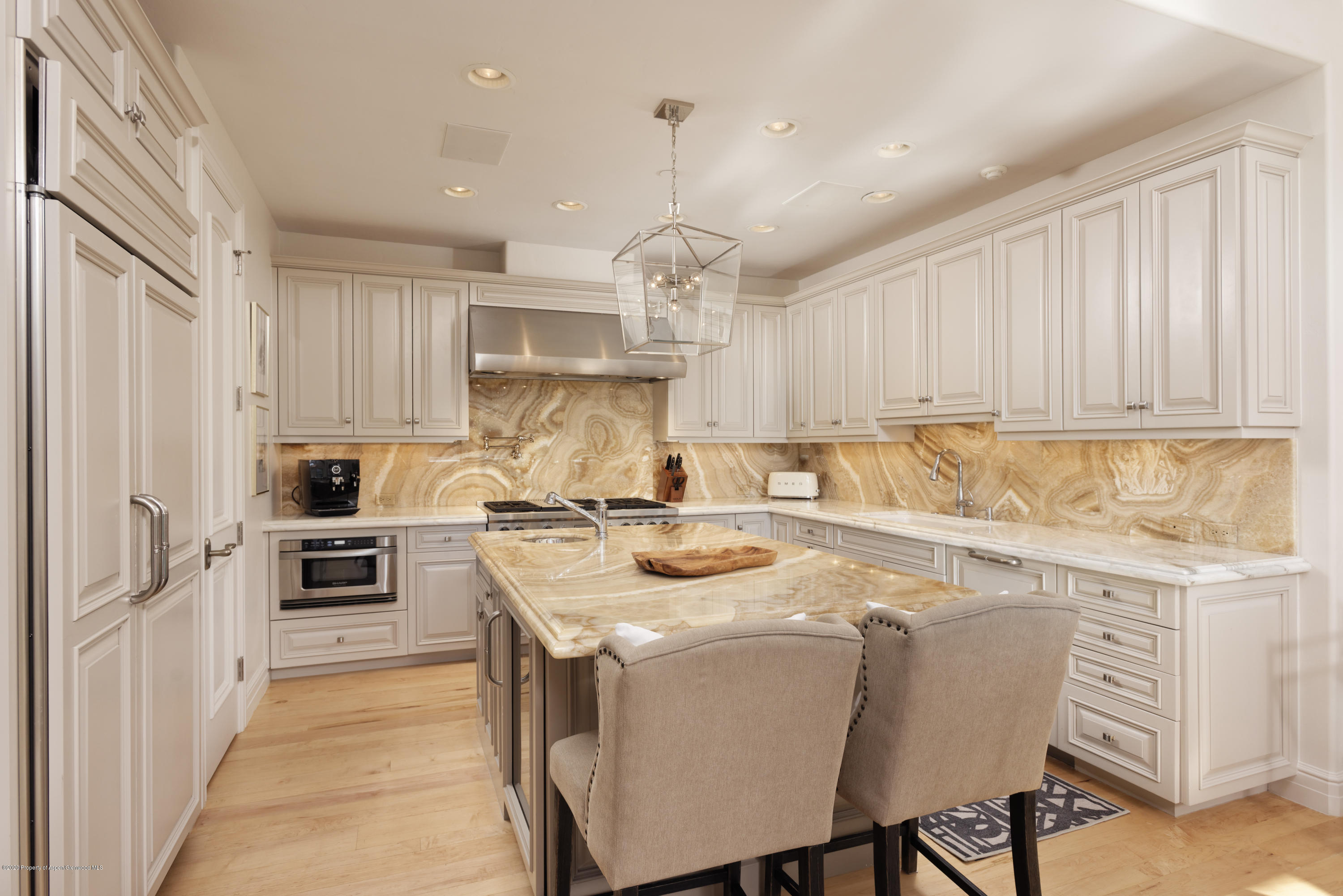 Kitchen with cream cabinetry, dramatic golden stone surfaces, and a large island with seating.