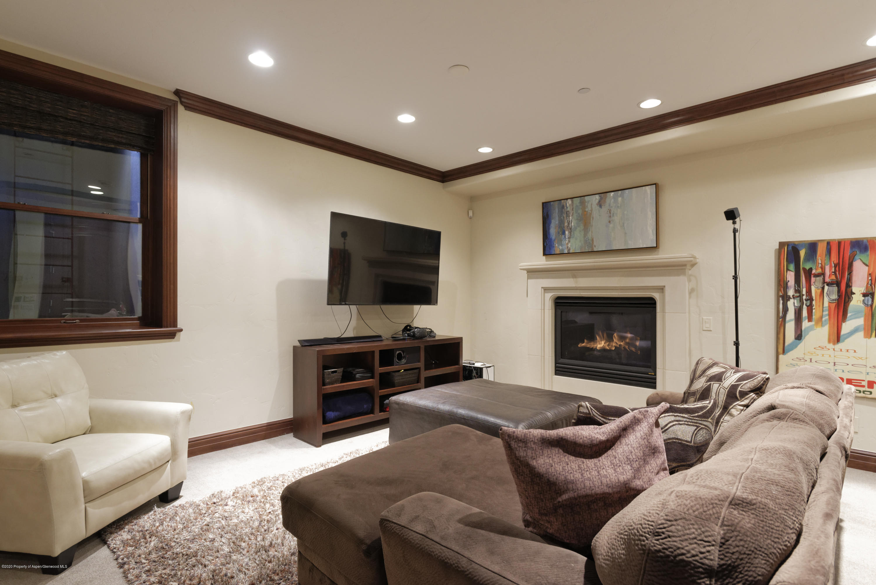 Furnished living room with a brown sectional, wall-mounted television, and lit gas fireplace.